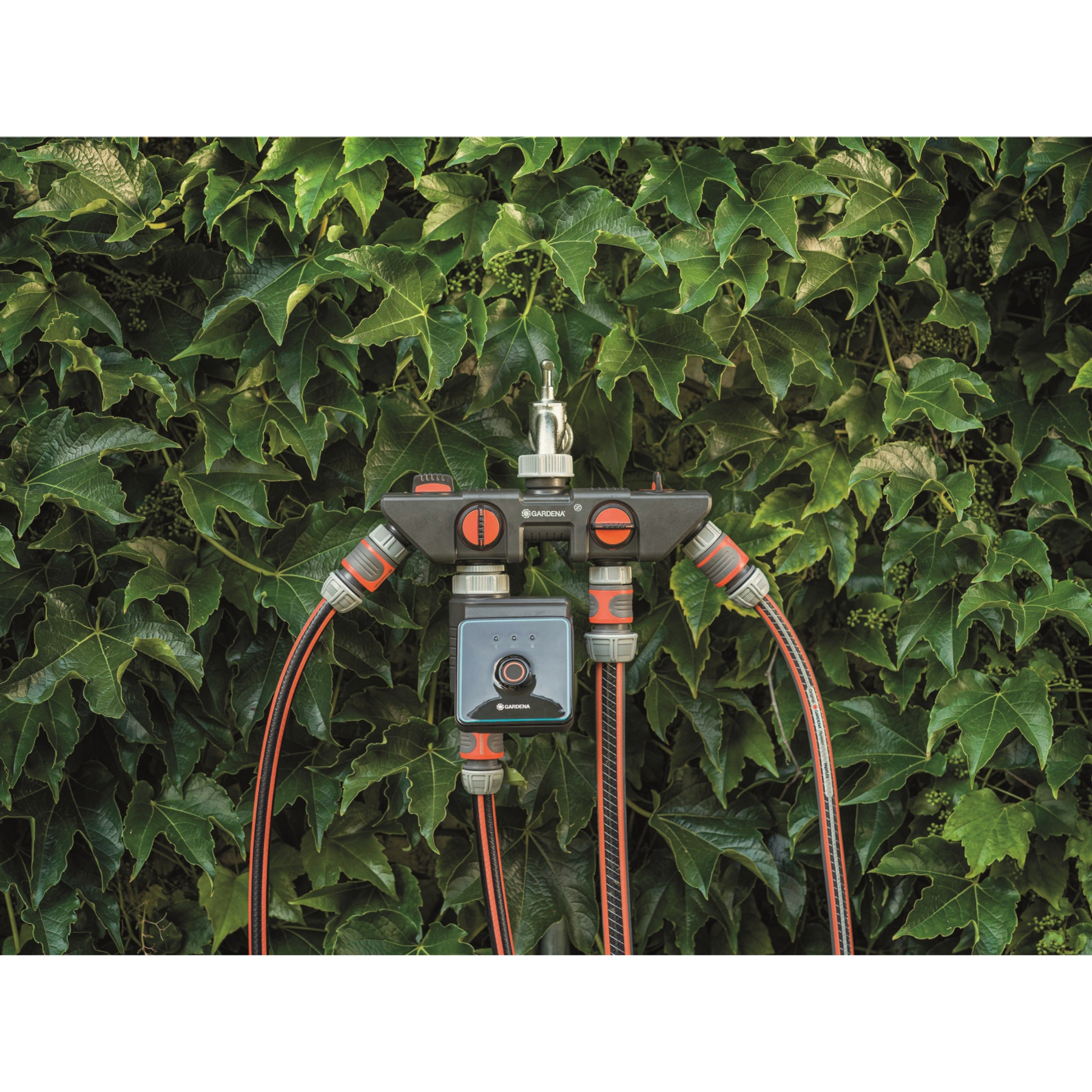 Ein Gardena-Bewässerungssteuerungssystem mit Schläuchen vor dem Hintergrund grüner Blätter.