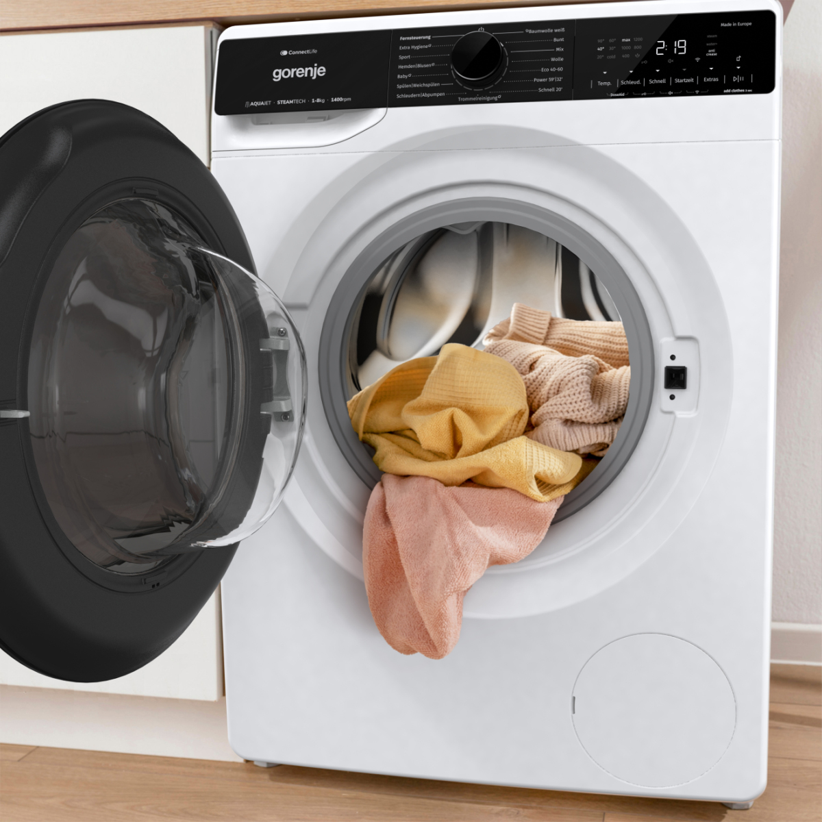 Eine weiße Gorenje-Waschmaschine mit offener Tür, die bunte Kleidung im Inneren zeigt. Die offene Tür zeigt einen schwarzen Rand.