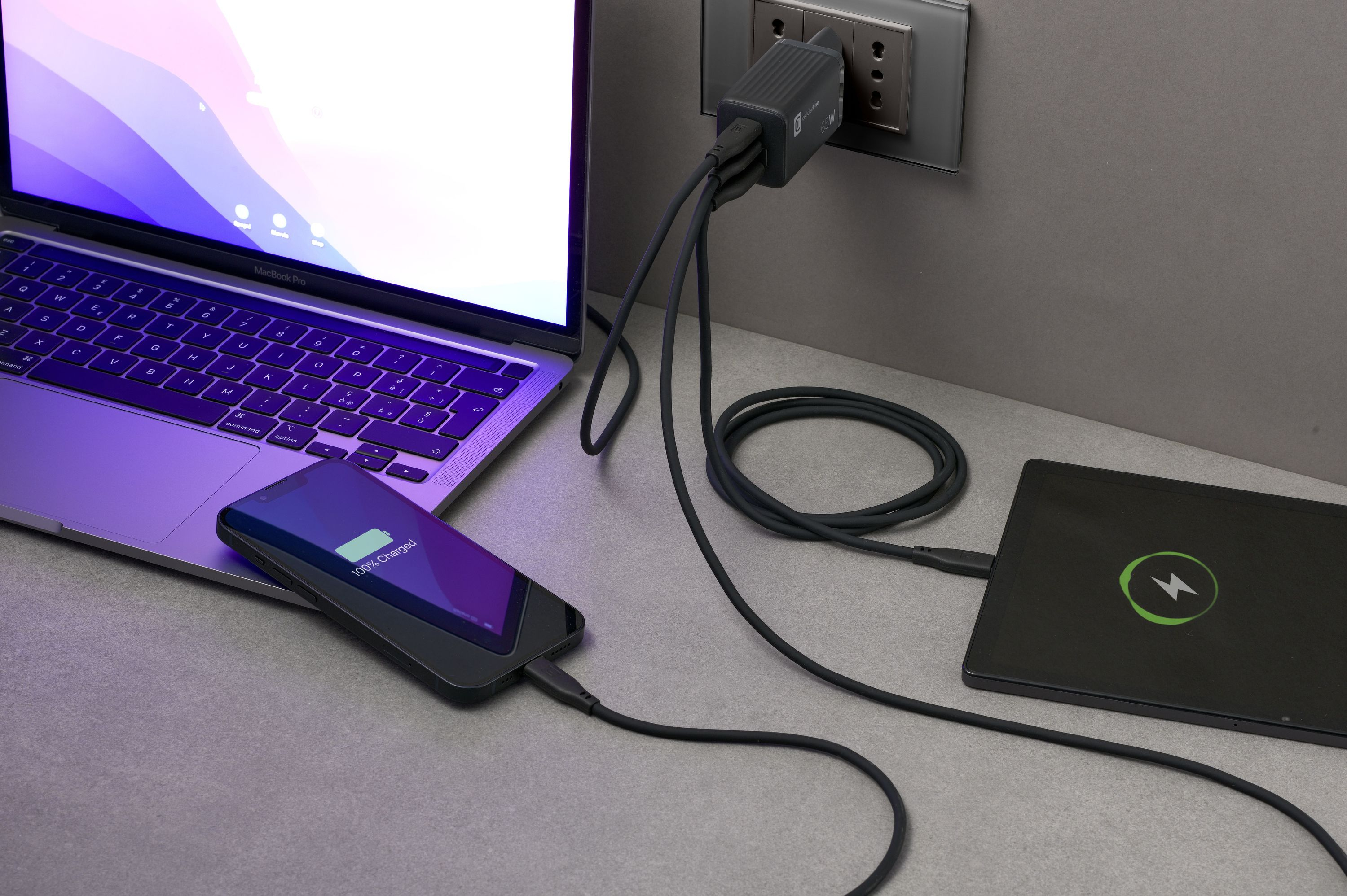 Laptop, Telefon und Tablet laden. Telefon zeigt 100% geladen. Tablet mit Blitzlogo. Ladegerät eingesteckt.