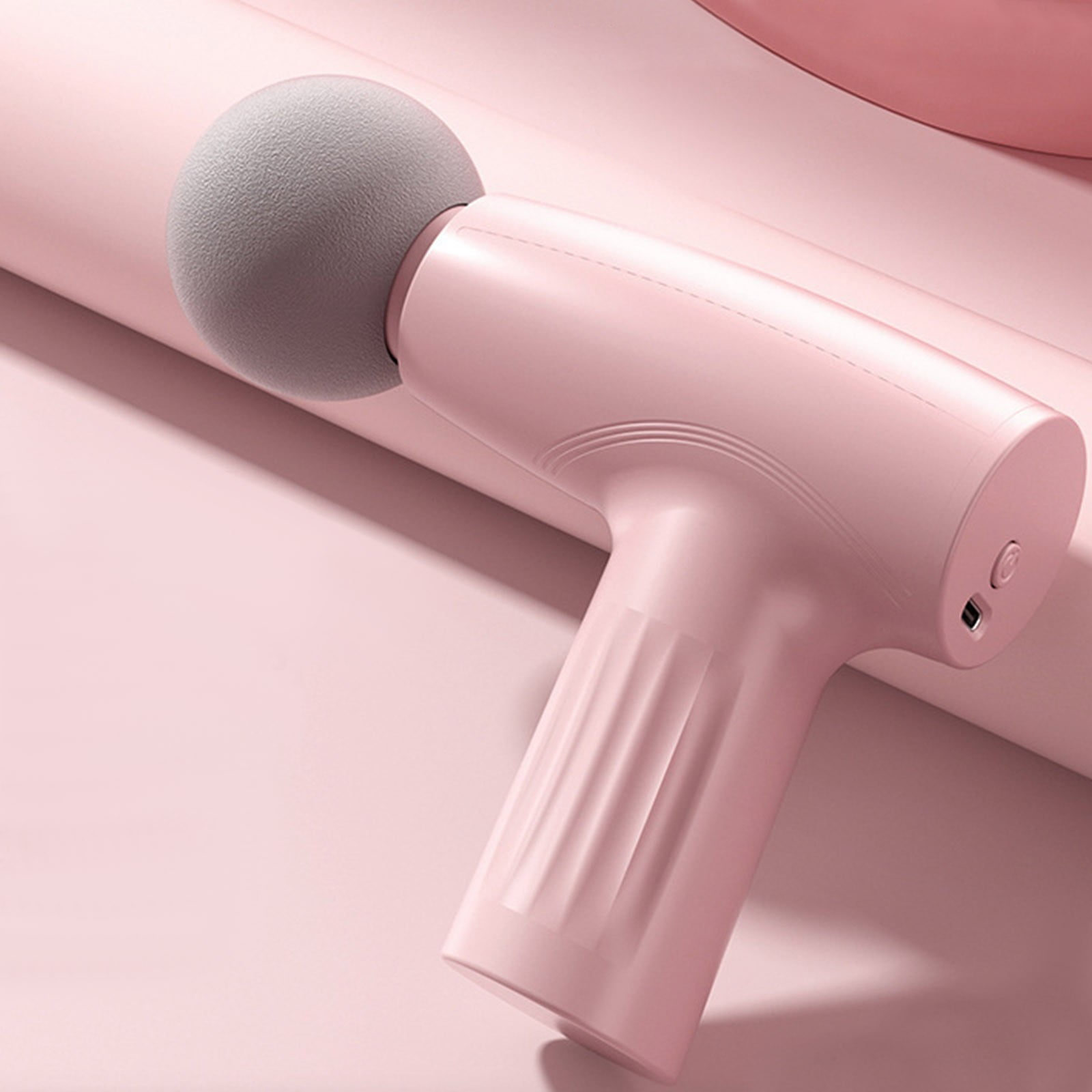 Eine rosa Massagepistole mit grauem kugelförmigem Kopf vor rosa Hintergrund. Details: Ein-Aus-Schalter und gerippter Griff.