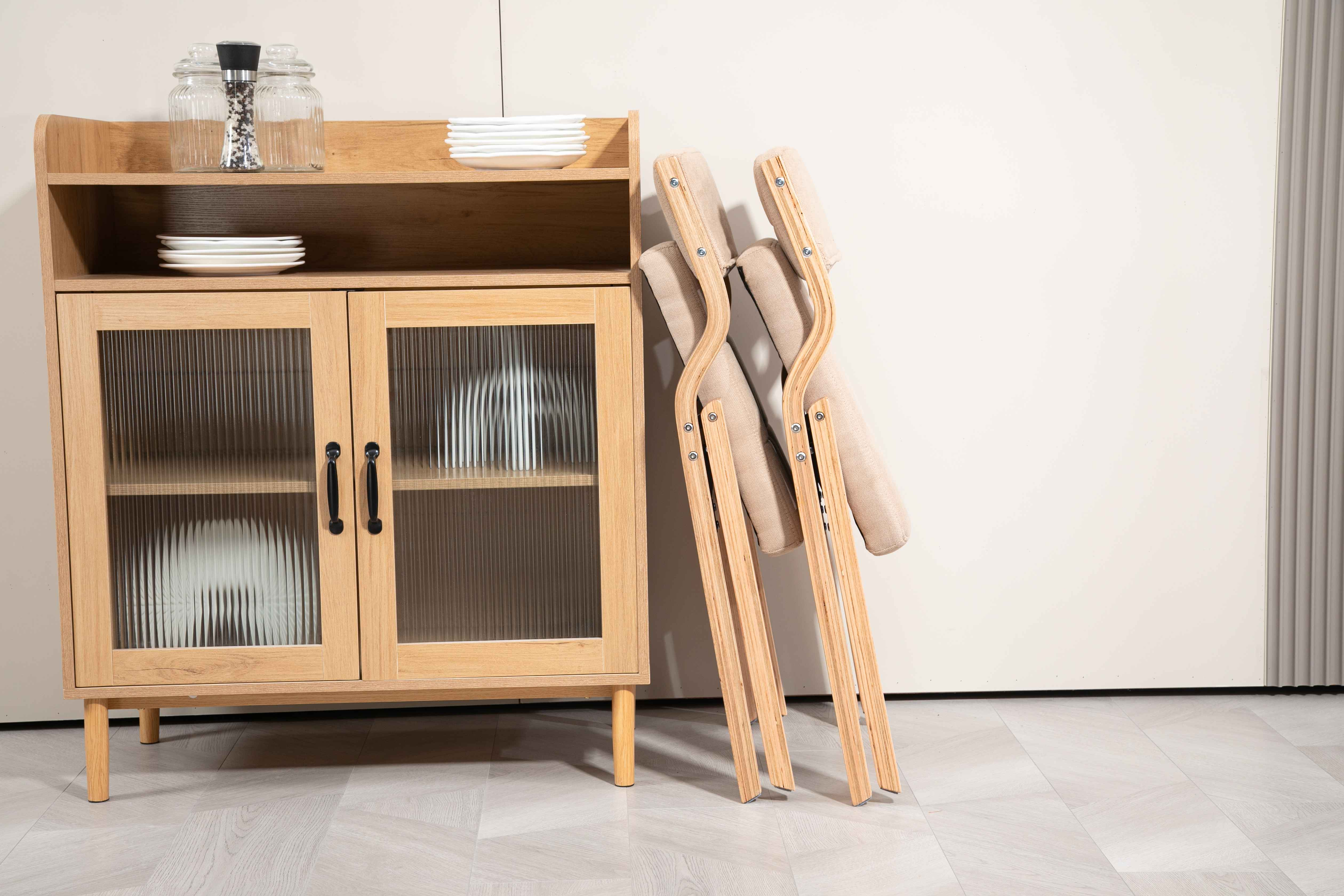 Ein Holzschrank mit Glastüren und Tellern, zwei zusammengeklappte Stühle lehnen an einer weißen Wand.