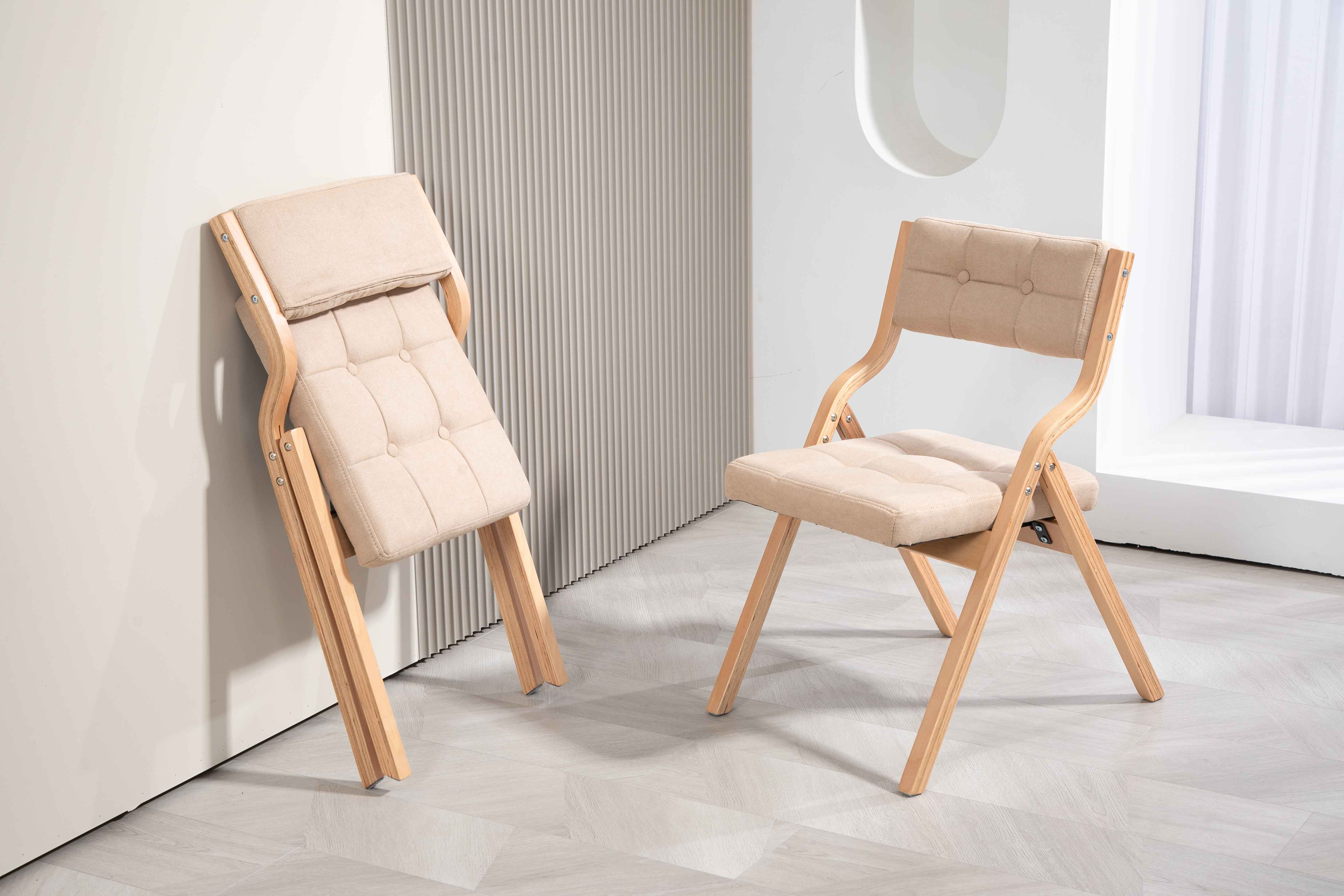 Zwei beige Klappstühle auf hellem Holzboden. Einer ist zusammengeklappt, der andere offen. Hintergrund hat strukturierte Wand und Fenster.