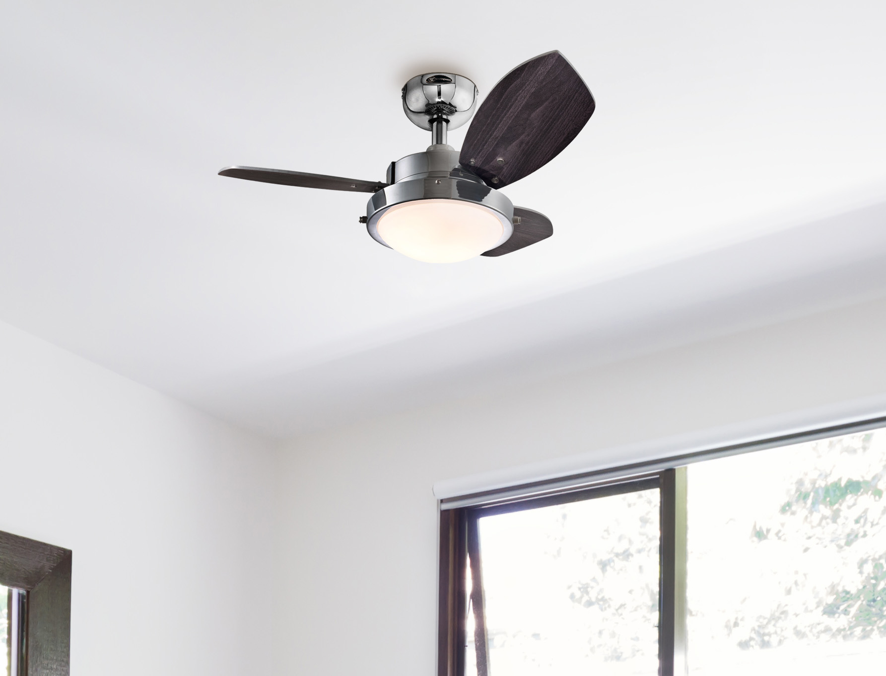 Ein Deckenventilator mit dunklen Holzflügeln und einer Leuchte ist an einer weißen Decke montiert. Unten ist ein Fenster zu sehen.