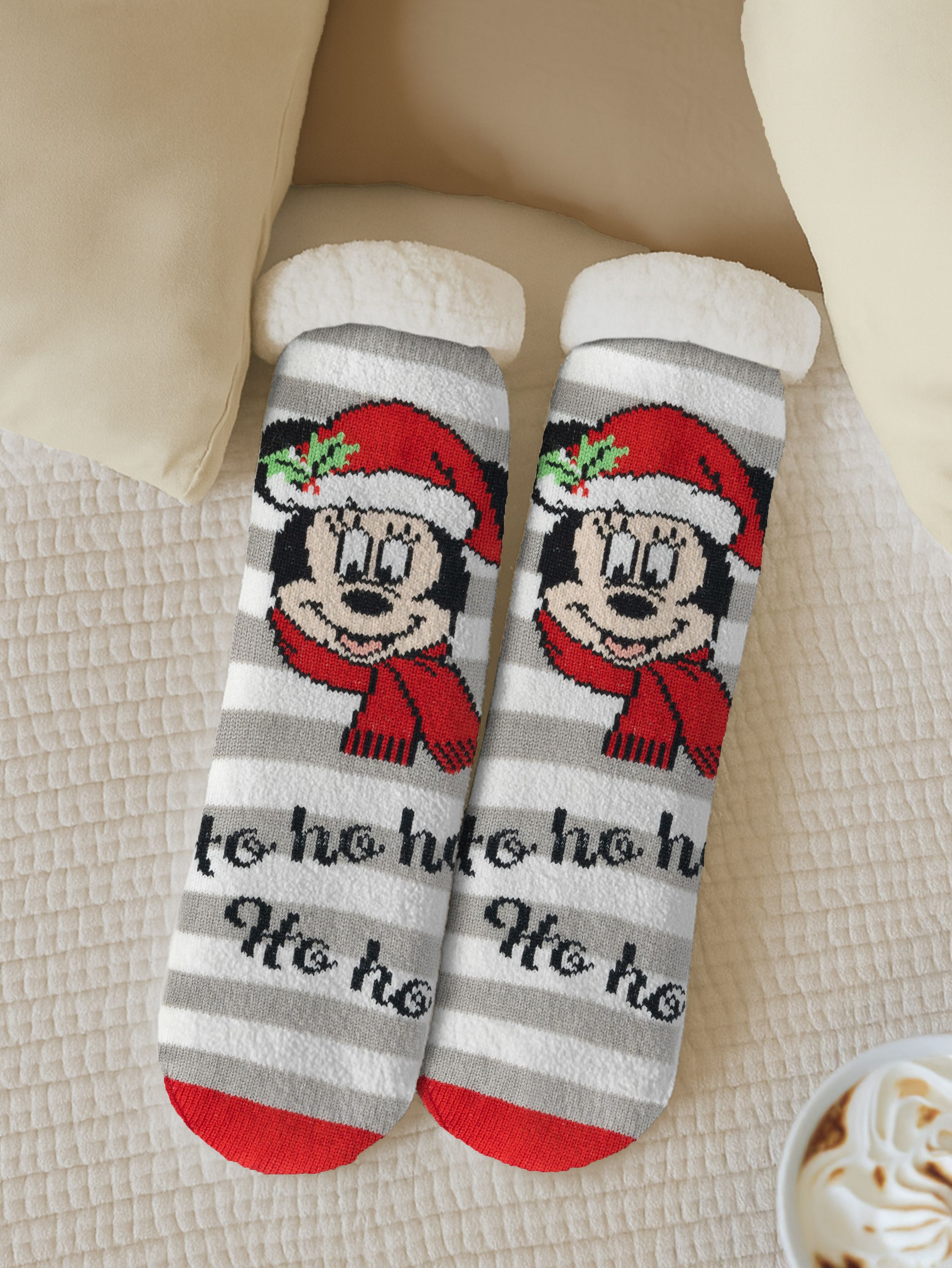 Zwei Weihnachtssocken mit Mickey Mouse. Die Socken liegen auf einem Bett mit Kissen.