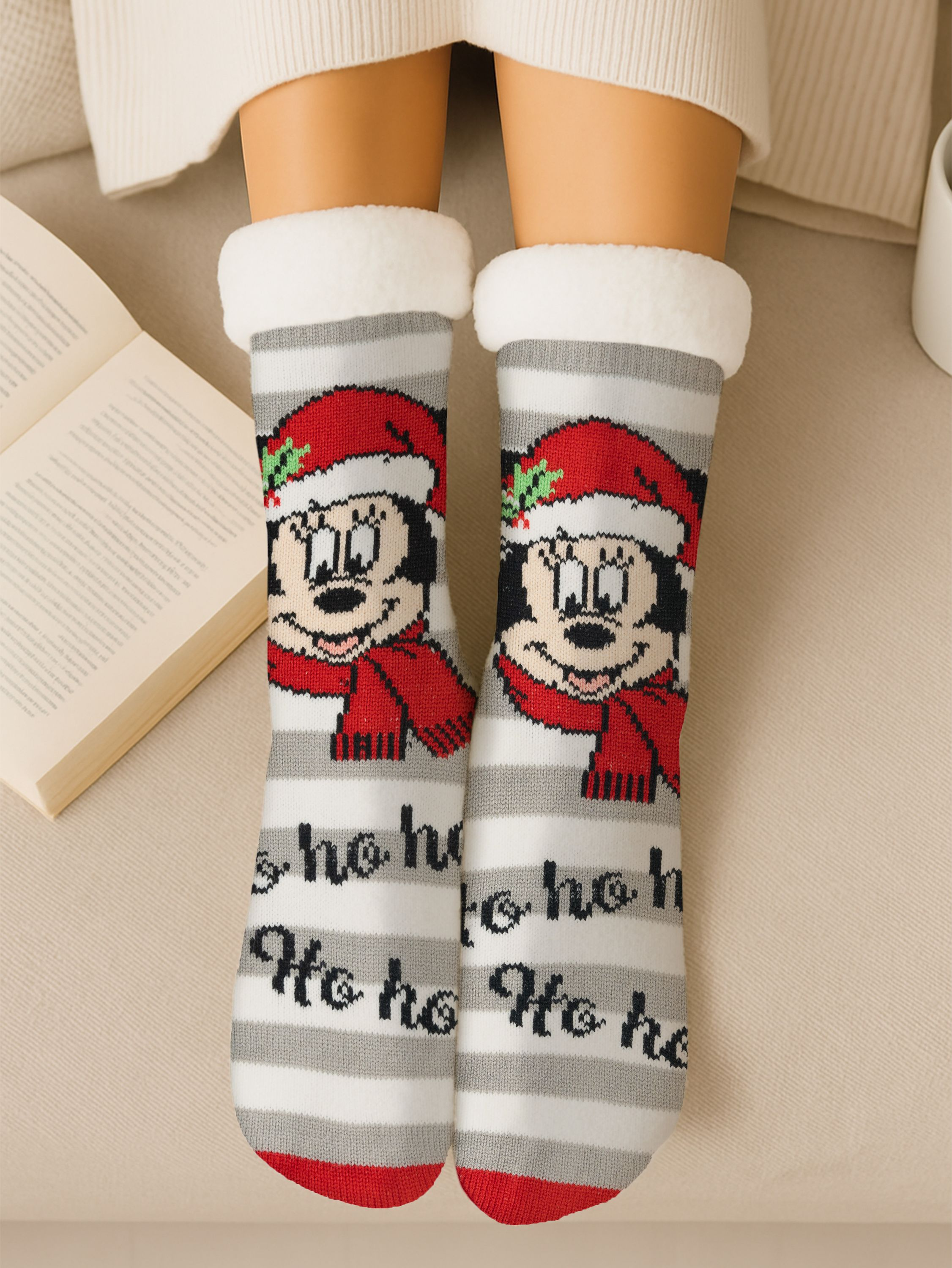 Person trägt Weihnachtssocken mit Mickey Mouse. Buch und Tasse im Hintergrund. Socken sind grau, rot und weiß.