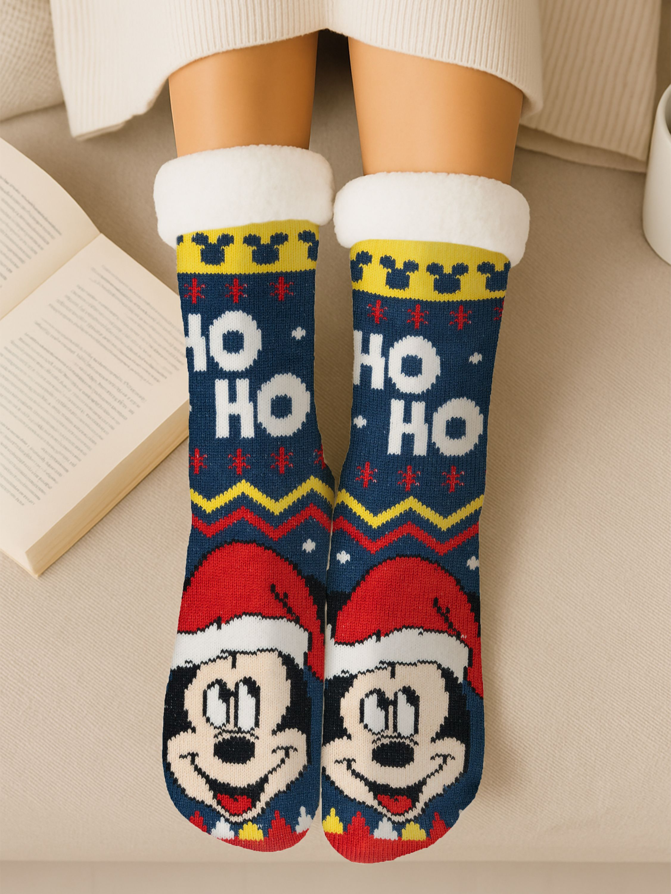 Beine mit Weihnachtssocken mit Mickey Mouse-Design. Links ist ein Buch geöffnet. Der Hintergrund ist hell.