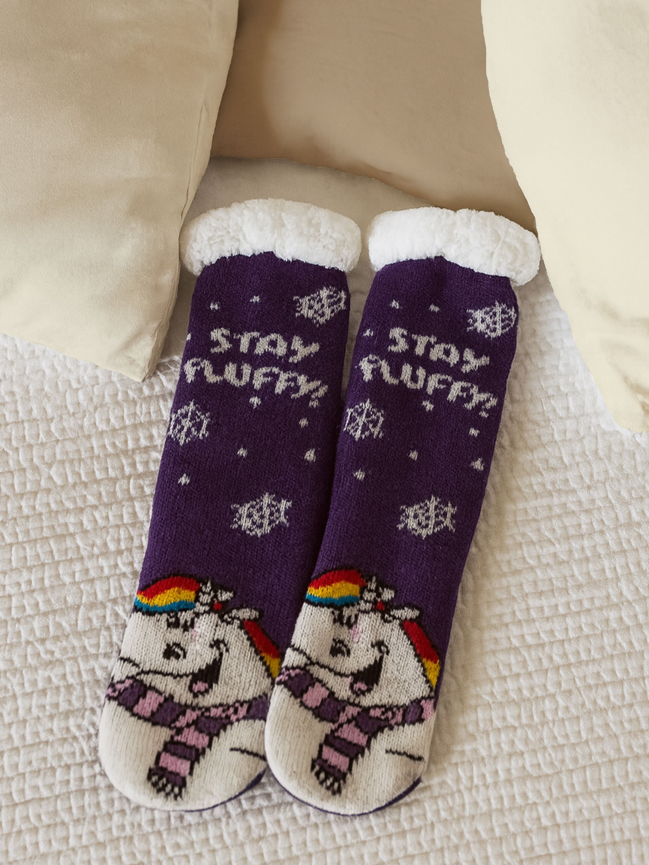 Lila Socken mit Einhorn-Design. Sie haben oben weißen Flaum und liegen auf einem weißen Bett.