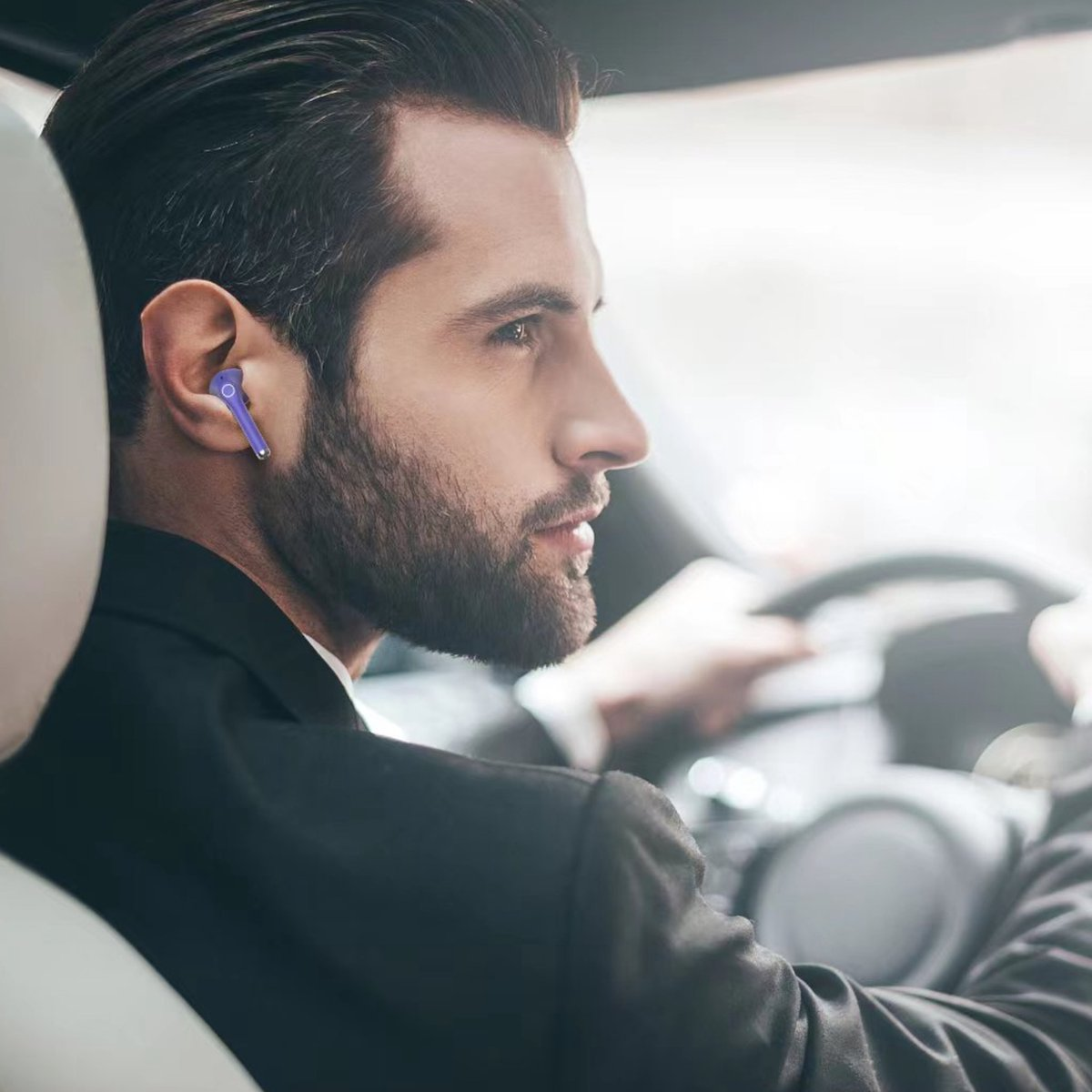 A man wearing a suit and earbuds is driving a car, with a focused expression. The car's interior is visible.
