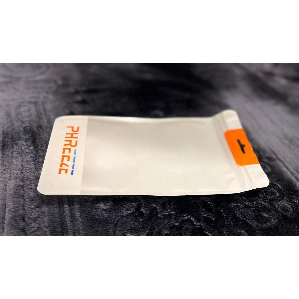 A white packet with an orange seal. The packet is on a black fuzzy surface. The text "PHRECCE" is printed on the packet.