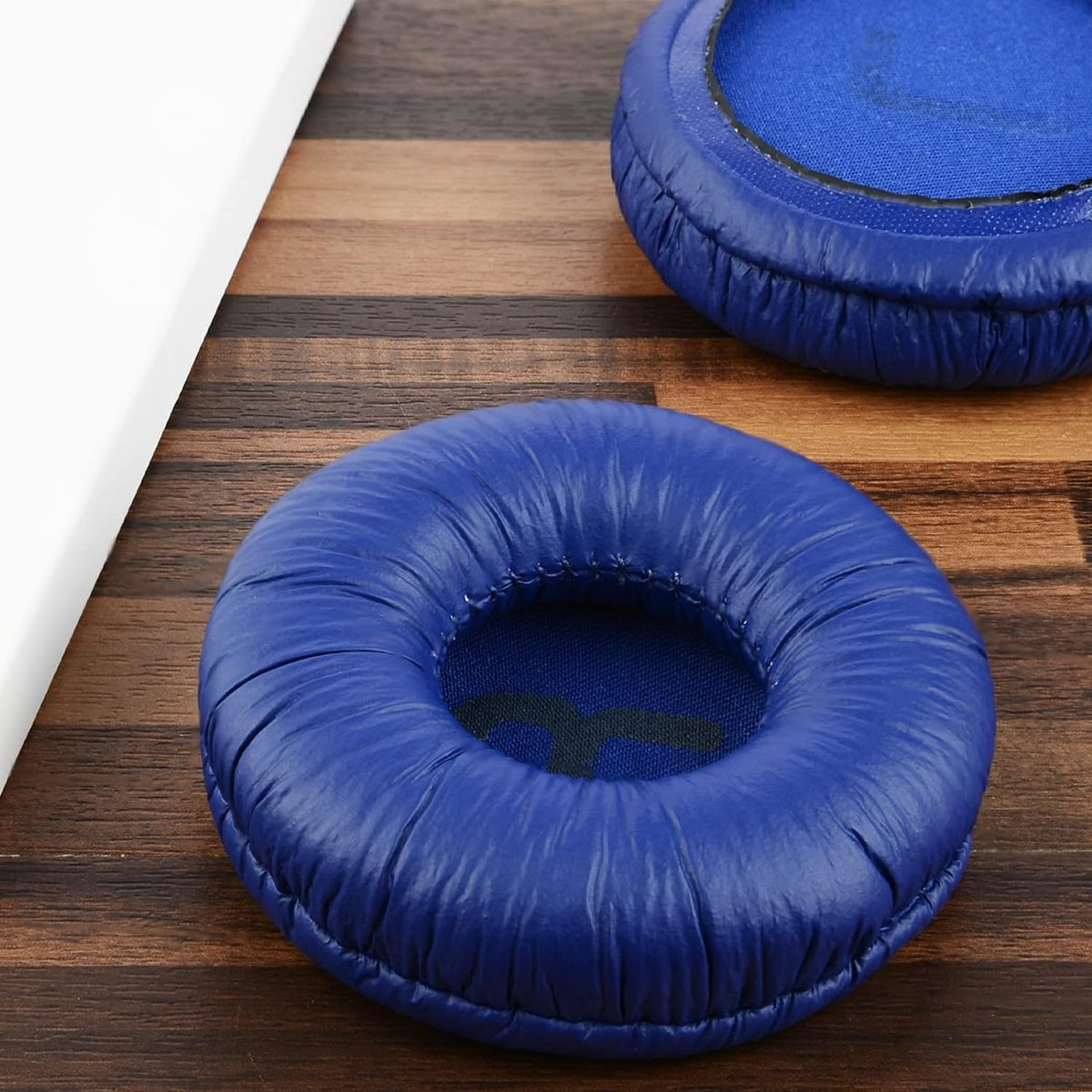 Twee blauwe oorkussens voor hoofdtelefoons op een houten oppervlak. Eén kussen is scherp, de andere is iets wazig op de achtergrond.