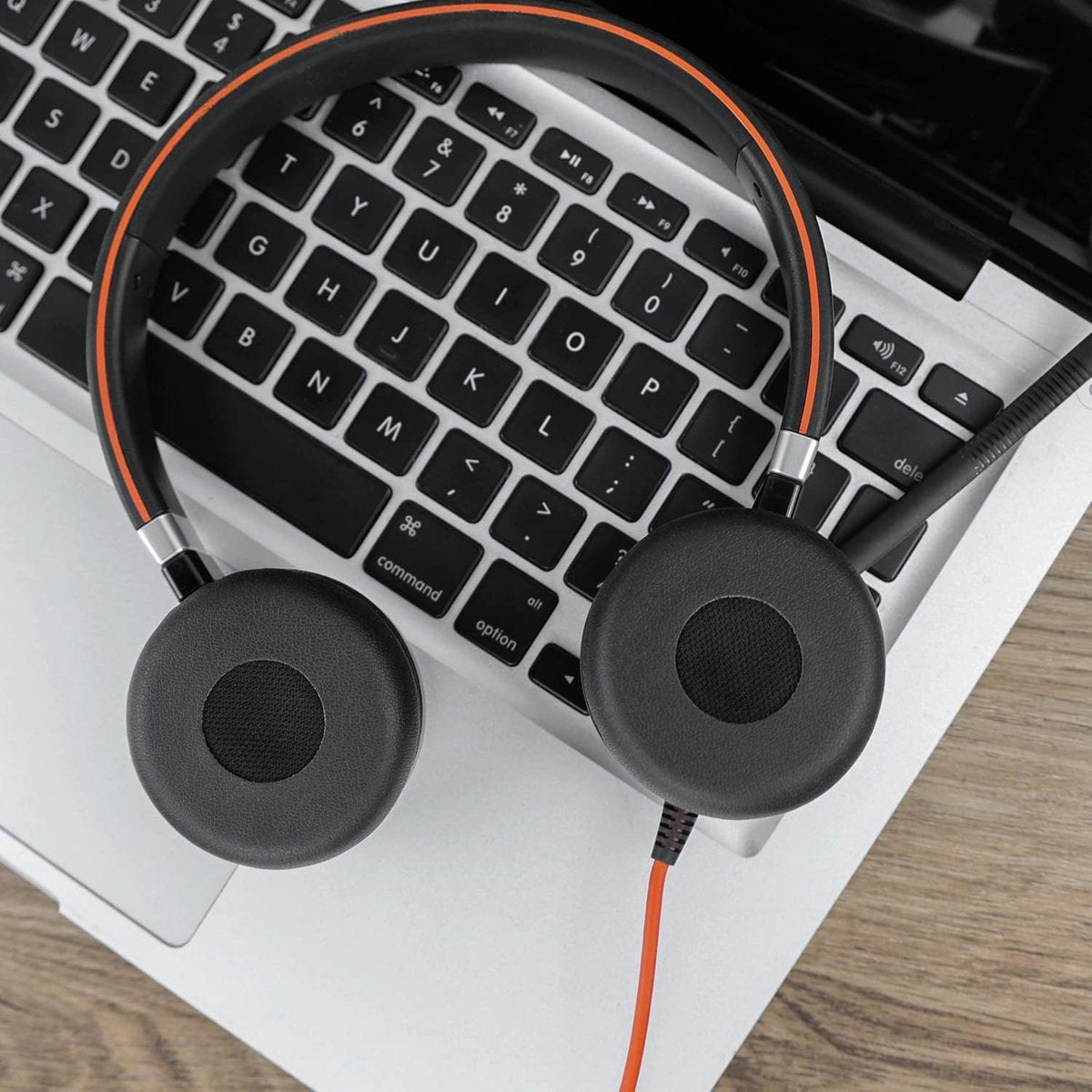Zwarte headset met oranje accenten op een laptoptoetsenbord. De headset ligt op het toetsenbord, met een oranje kabel.