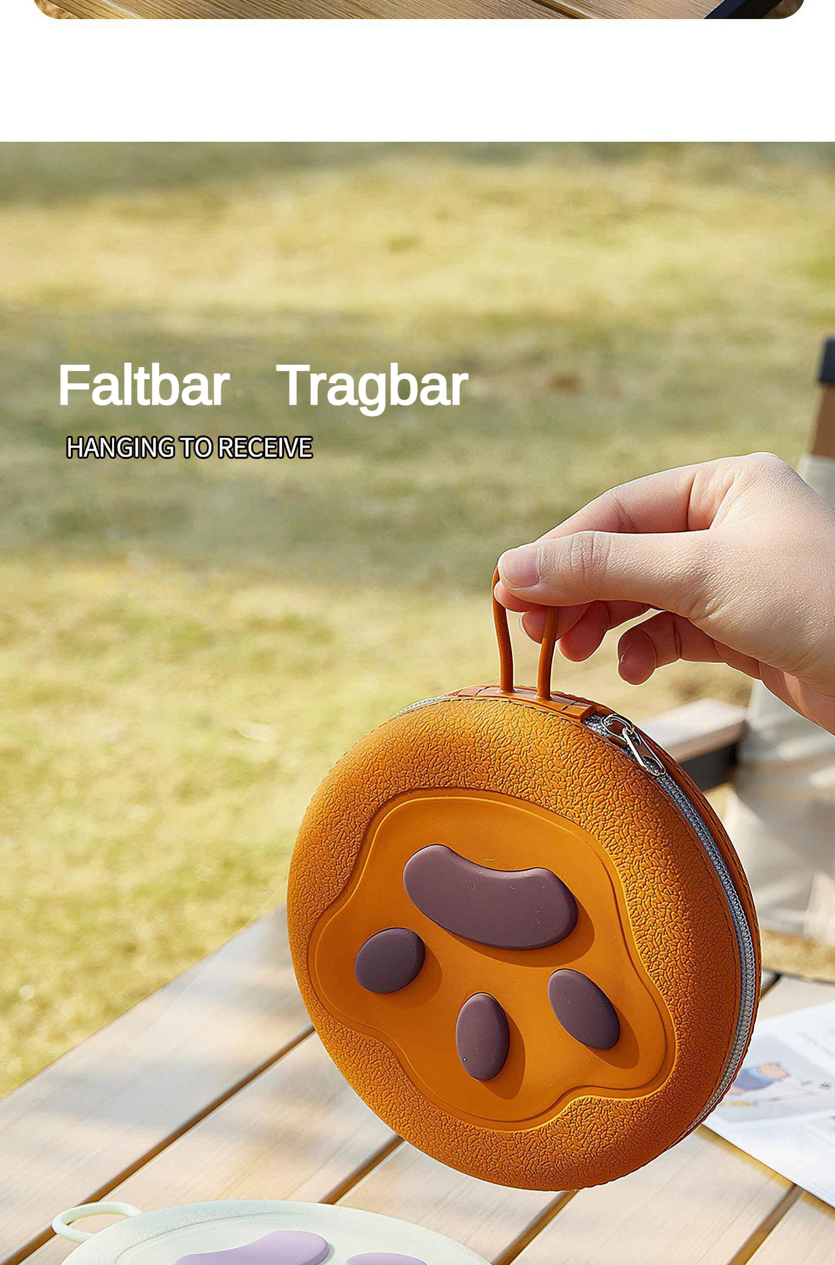 Eine orangefarbene Pfotenabdrucktasche wird von einer Hand hochgehalten. Die Tasche liegt auf einem Holztisch, mit Gras im Hintergrund.