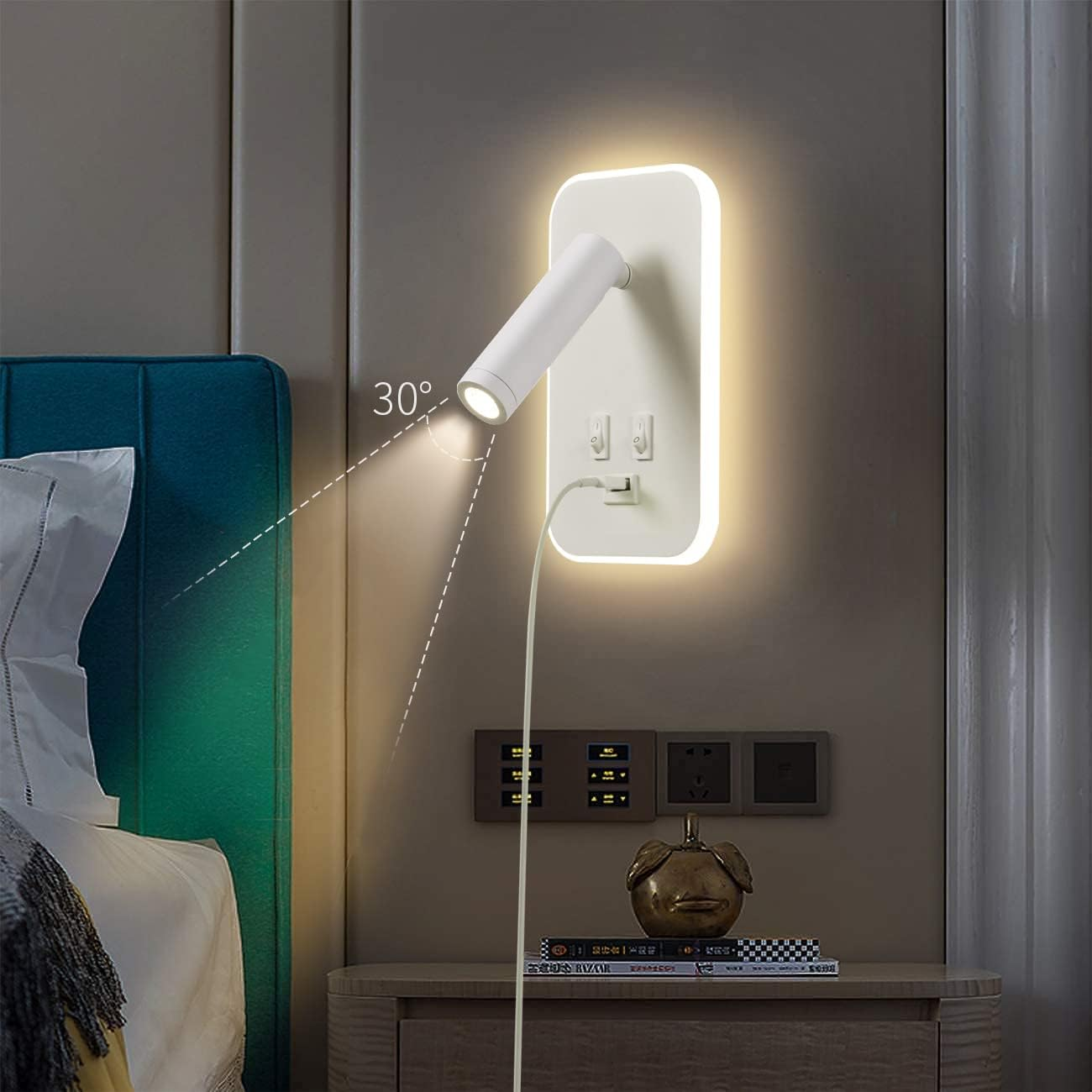 Eine an der Wand befestigte Leselampe strahlt Licht aus. Links ist ein Bett mit tealfarbenem Kopfteil. Darunter hat ein Nachttisch Dekor und eine Steckdose.