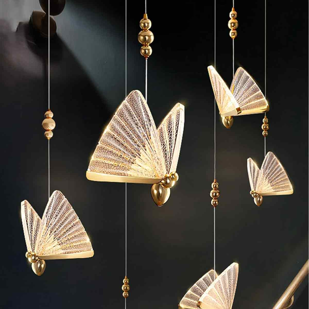 Goldene, schmetterlingsförmige Lichter hängen von der Decke. Dunkler Hintergrund. Lichter haben komplizierte Muster und sind beleuchtet.