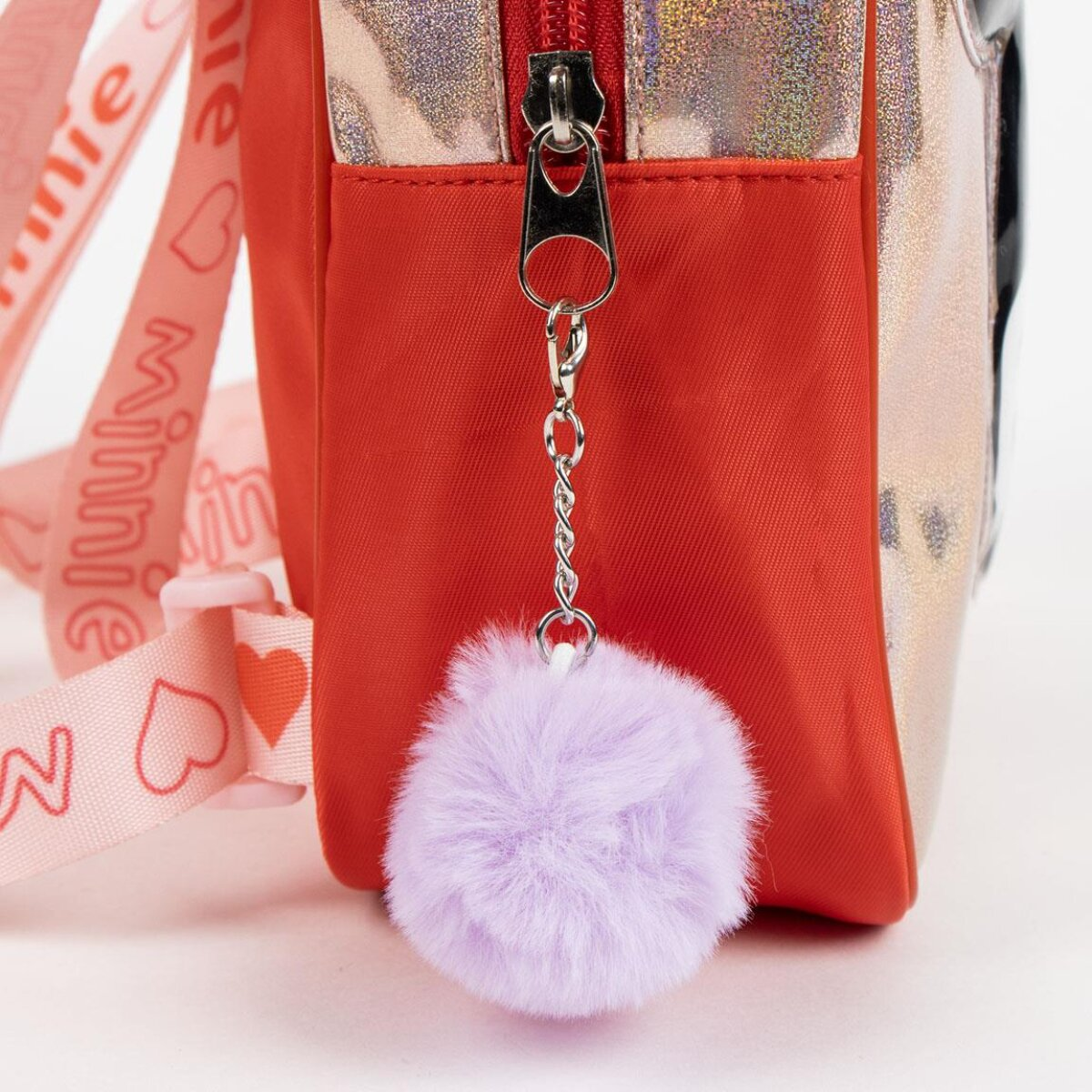 Roter Rucksack mit silbernem Reißverschluss und lila flauschigem Schlüsselanhänger. Rosa Minnie Mouse-Träger sind sichtbar.