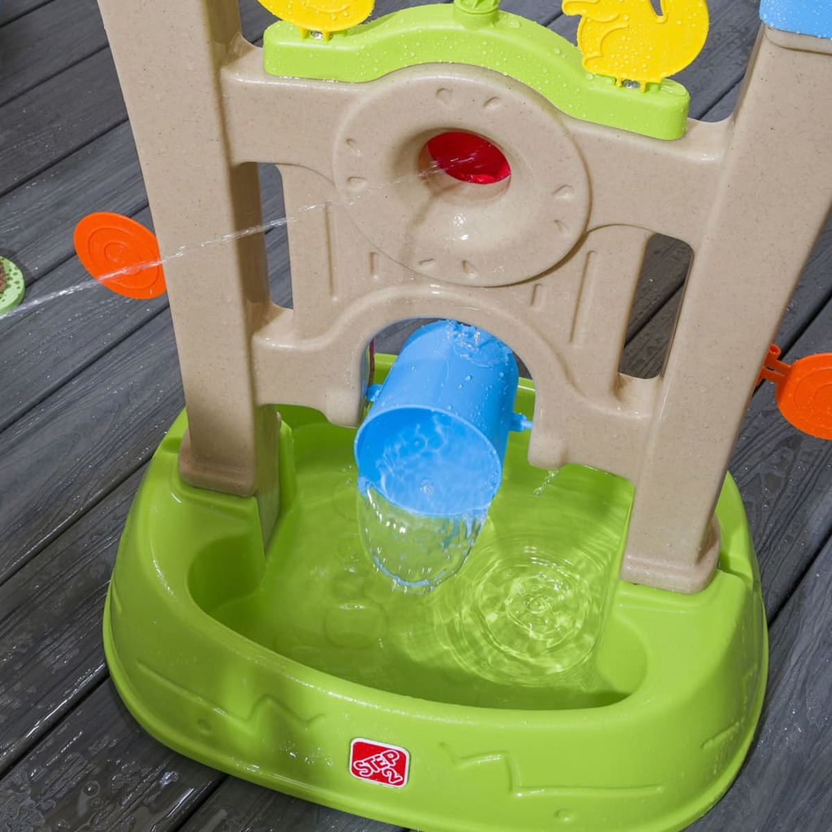 Ein Wassertisch mit fließendem Wasser. Ein blauer Eimer gießt Wasser in ein grünes Becken. Orange und gelbe Dekorationen sind oben.