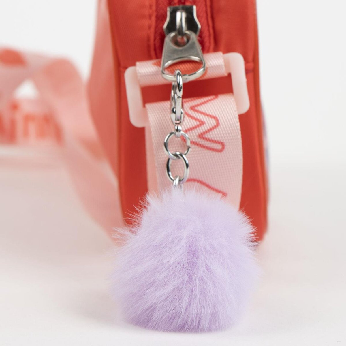 Una bolsa roja con cremallera, una correa rosa y un llavero de bola peluda morada. El fondo es blanco.