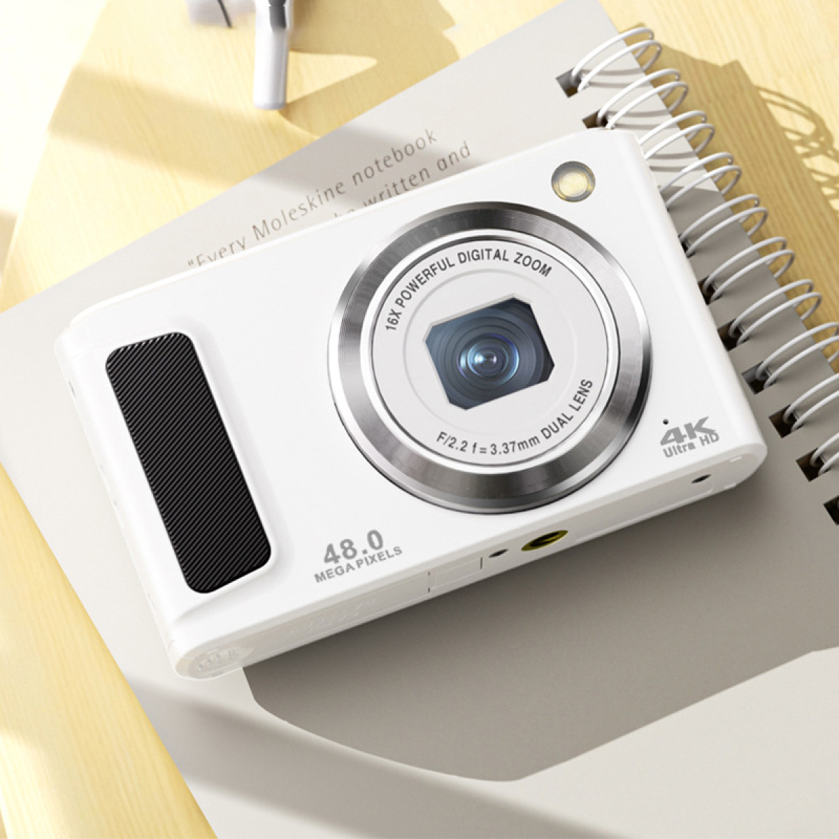 Eine weiße Digitalkamera mit großem Objektiv und schwarzem Griff liegt auf einem Notizbuch. Die Kamera hat 48,0 Megapixel und 16-fach Zoom.