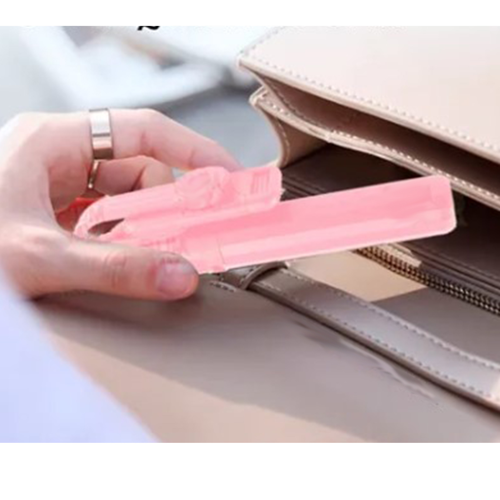 Eine Hand hält einen rosa Gegenstand, wahrscheinlich einen Lippenstift, in der Nähe einer beigen Handtasche. Ein silberner Ring ist an einem Finger.