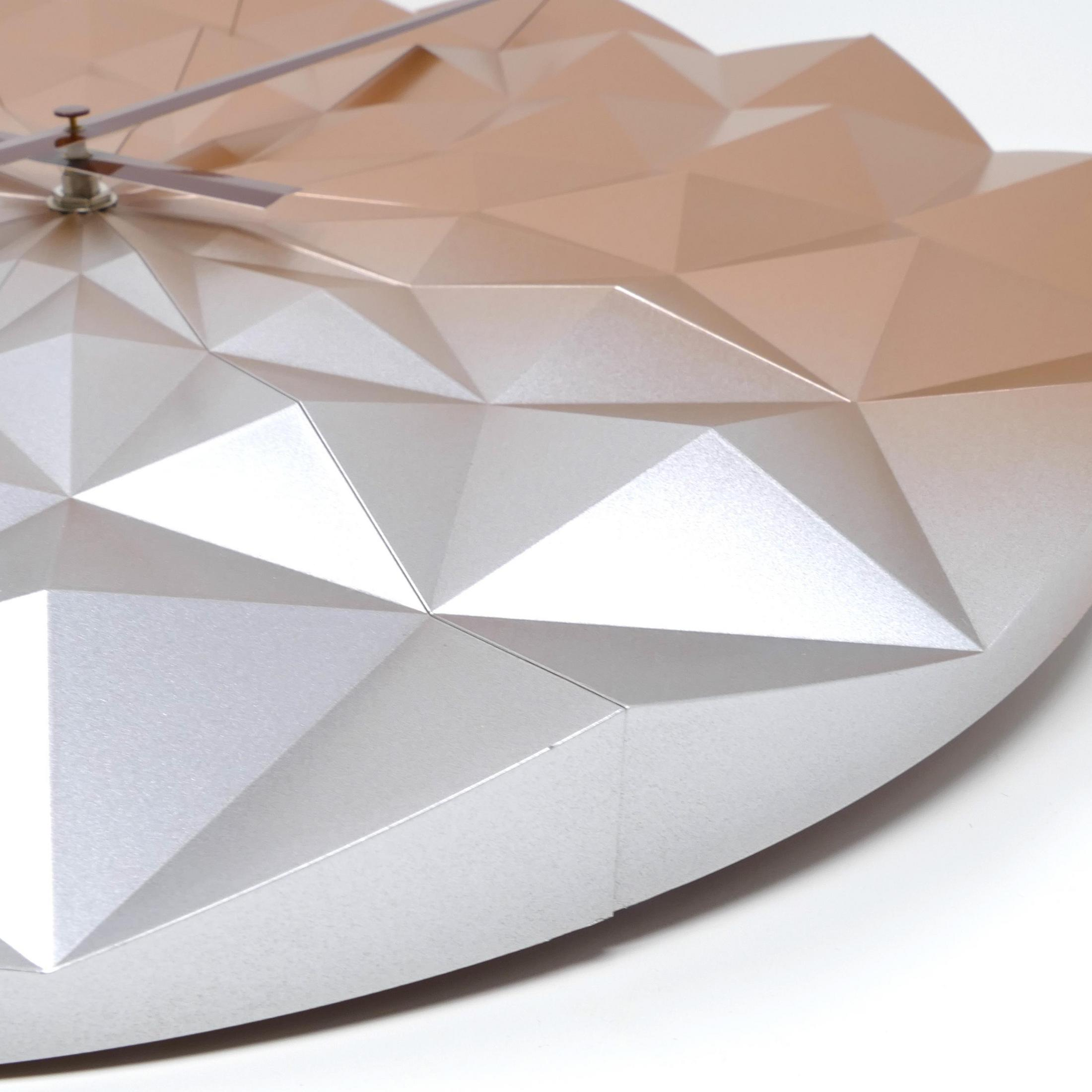 Eine moderne Uhr mit geometrischem Design. Das Zifferblatt ist silber und bronze, mit abgewinkelten Flächen und zwei Zeigern.
