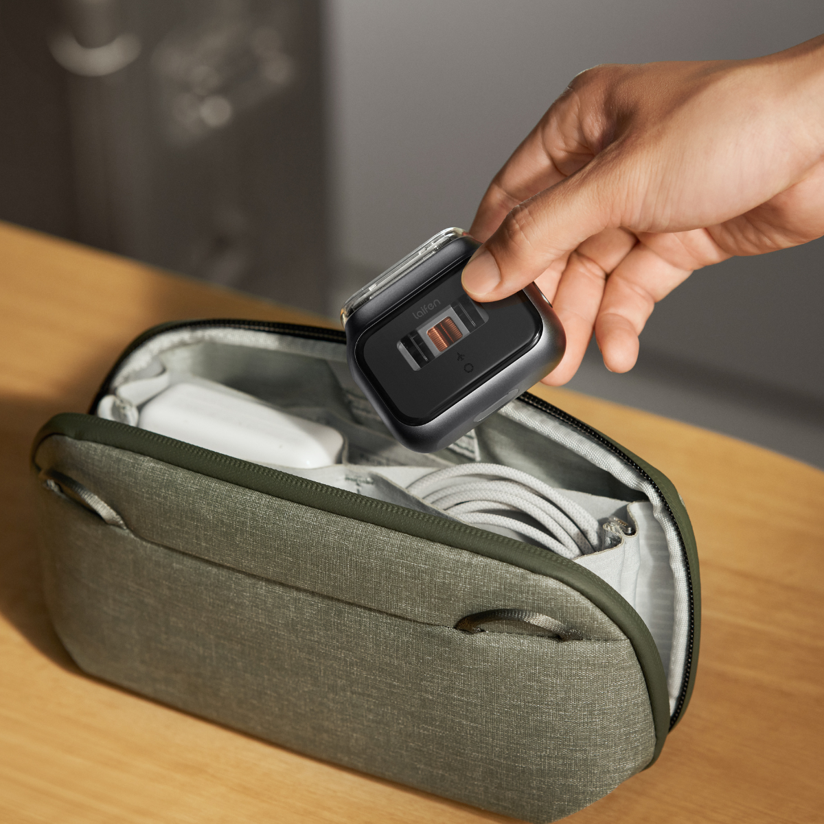 Une main tient un appareil noir au-dessus d'une trousse verte ouverte. À l'intérieur, des objets blancs et un câble gris.