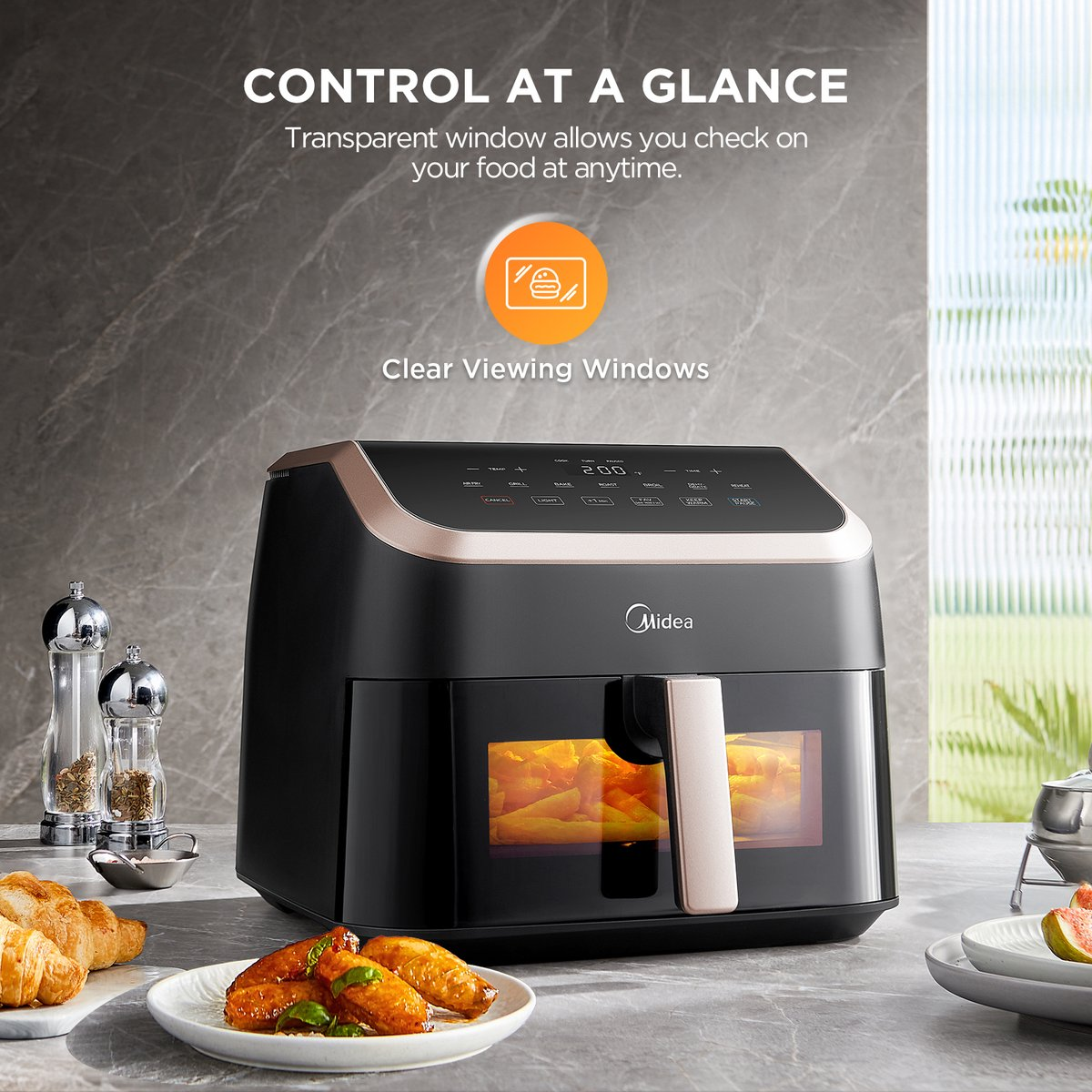 Friggitrice ad aria Midea nera con finestra trasparente. Piatto con ali e croissant. Saliera e sovrapposizione di testo.