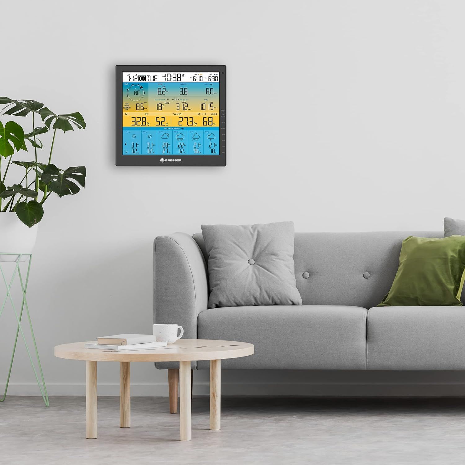 Ein Raum mit Sofa, Tisch und Wetterstation an der Wand. Die Wetterstation zeigt Temperatur und Wettervorhersagen an.
