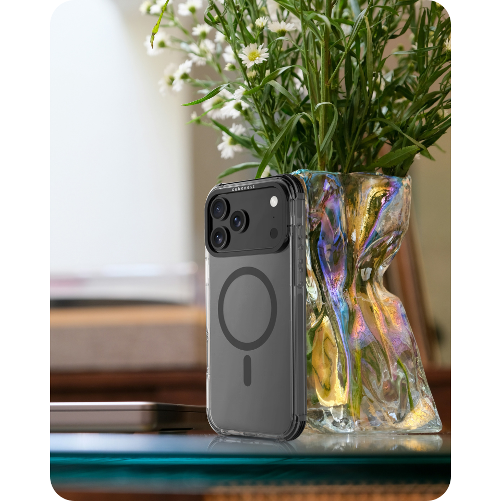 Ein iPhone in einer transparenten Hülle steht neben einer Vase mit Blumen. Die Vase hat einen irisierenden Effekt. Ein Tisch ist im Vordergrund.
