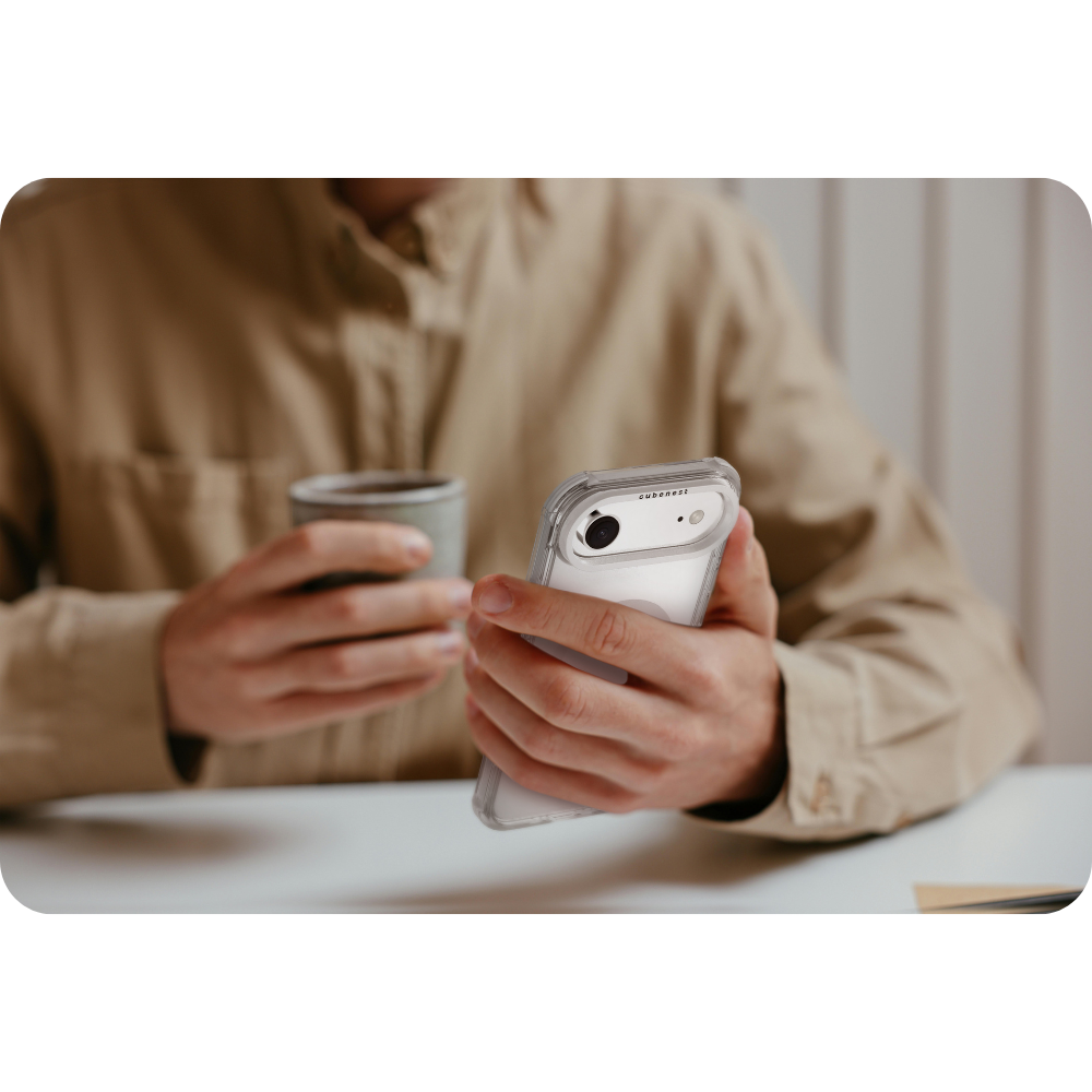 Eine Person hält ein Telefon in einer durchsichtigen Hülle und einen Becher. Der Hintergrund ist verschwommen.