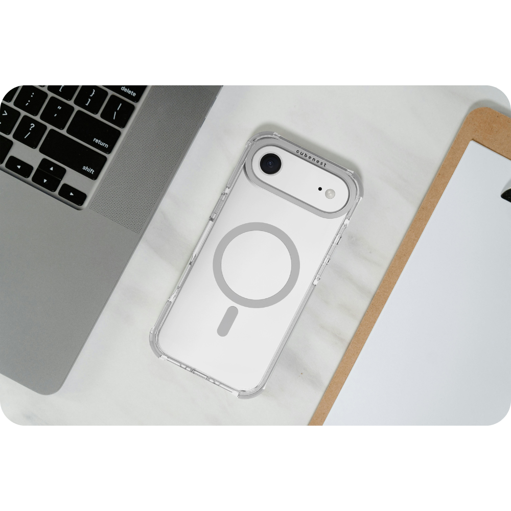 Eine transparente Handyhülle mit grauem Ring und Minuszeichen liegt auf einer Marmoroberfläche, zusammen mit einem Laptop und einem Klemmbrett.