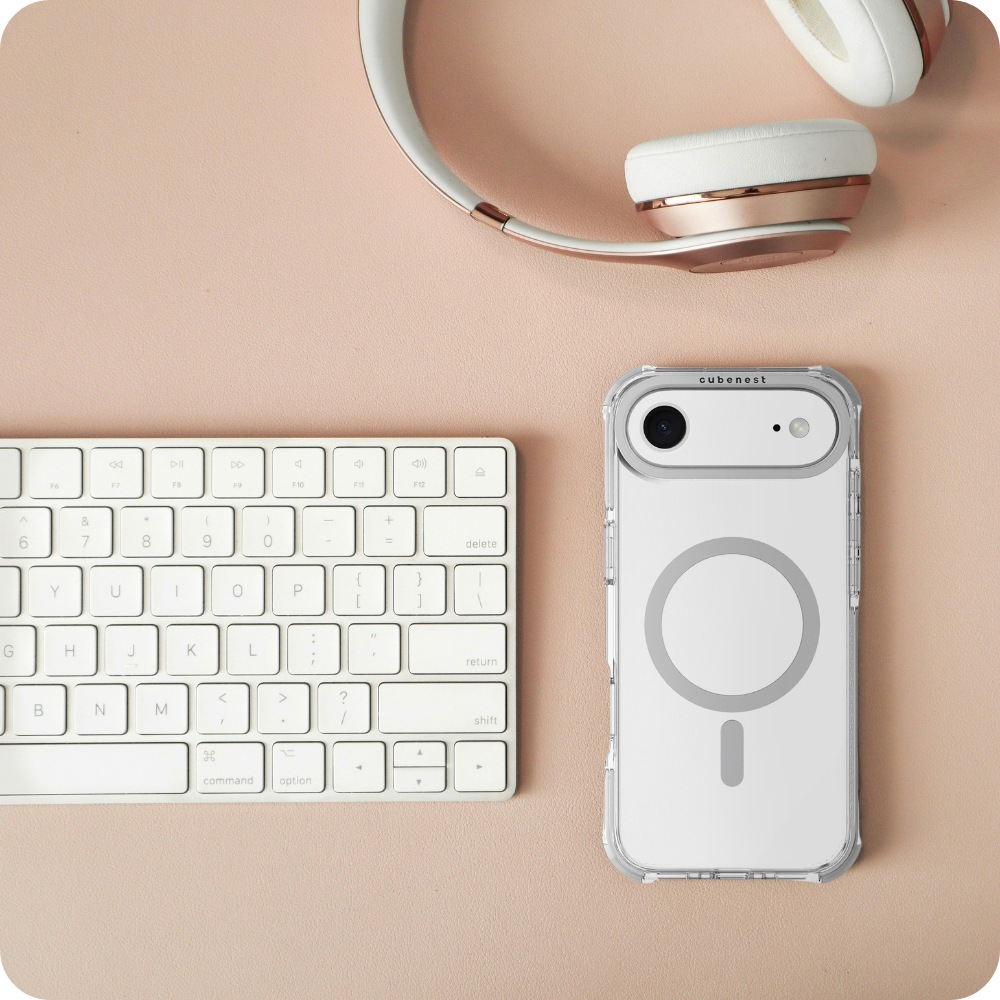 Eine weiße Tastatur, ein Telefon in einer durchsichtigen Hülle und Kopfhörer liegen auf einer rosa Oberfläche. Die Telefonhülle hat ein kreisförmiges Design.