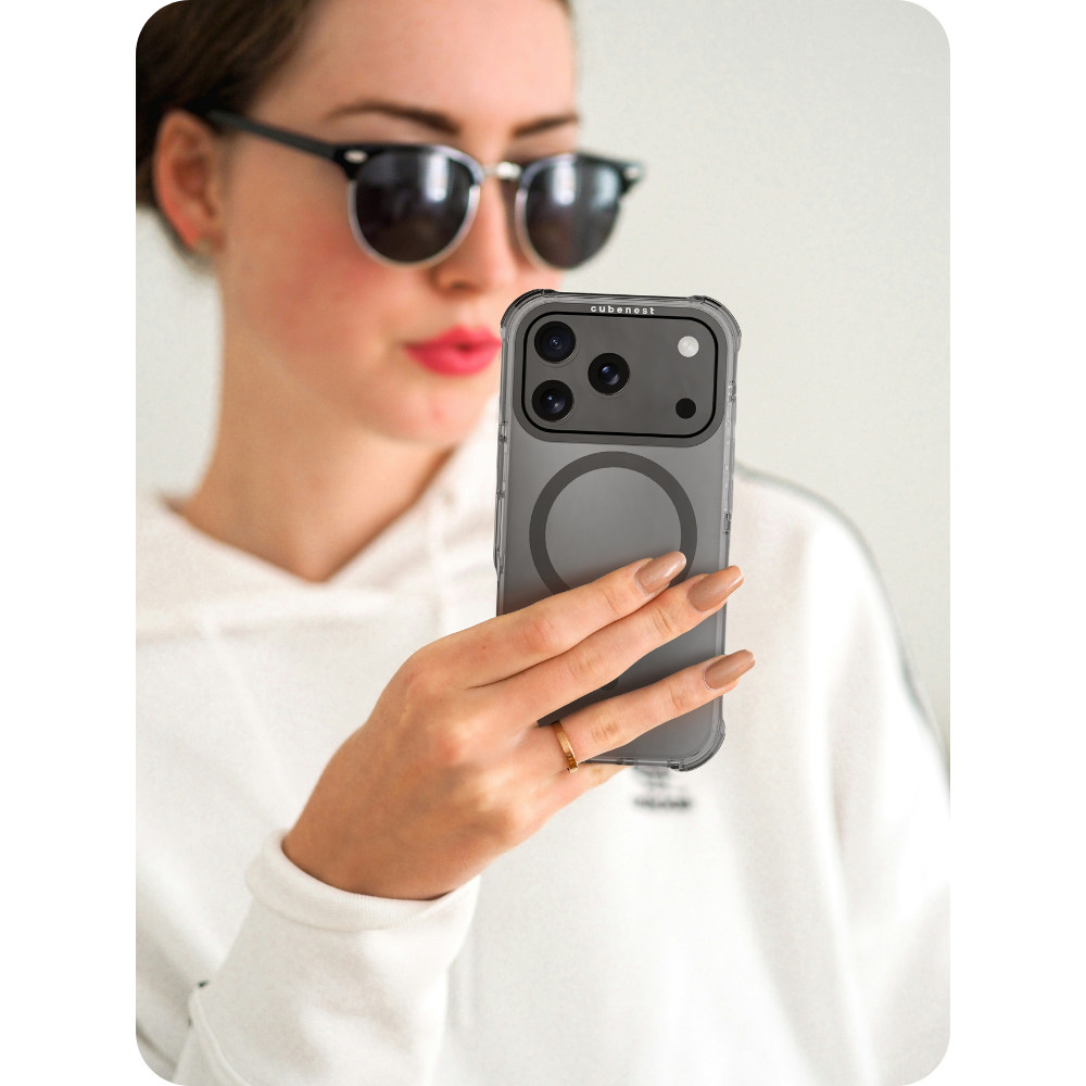 Frau mit Sonnenbrille hält ein Telefon in einer durchsichtigen Hülle. Das Telefon hat eine Kamera. Sie trägt einen weißen Kapuzenpullover.
