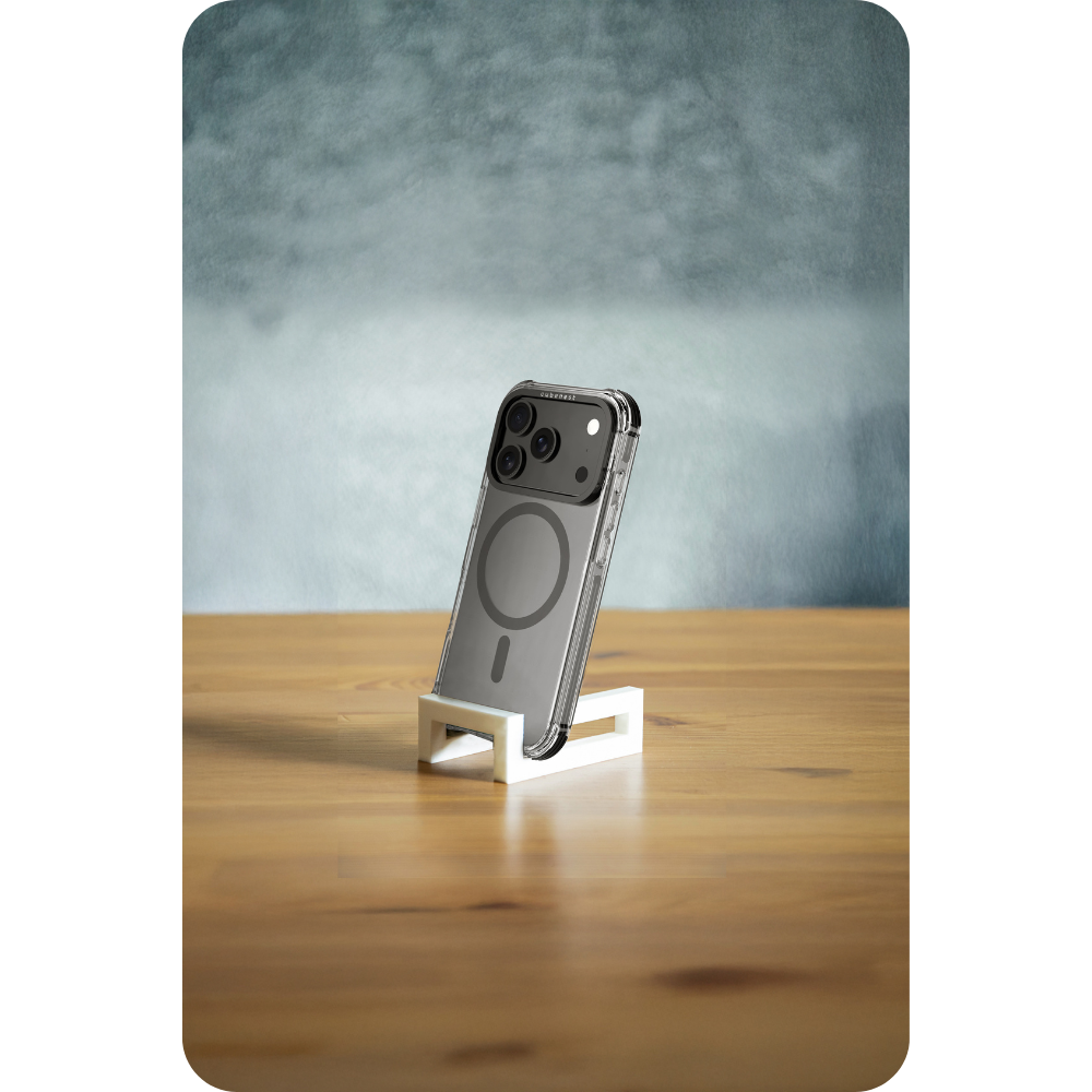 Ein iPhone in einer durchsichtigen Hülle steht auf einem weißen Ständer auf einem Holztisch. Ein hellblau-grauer Hintergrund ist hinter dem Telefon.