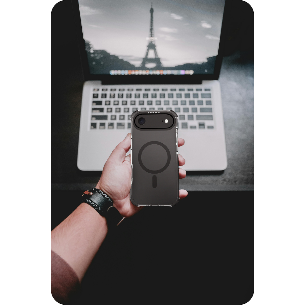 Mano che tiene una custodia per telefono con un design a cerchio nero. Un laptop sullo sfondo con un'immagine della Torre Eiffel.