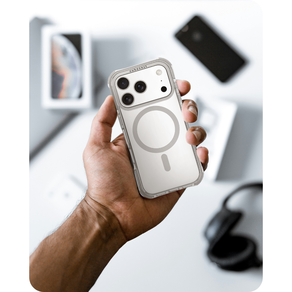 Eine Hand hält eine klare Handyhülle mit kreisförmigem Design. Weitere Objekte sind ein schwarzes Telefon, Kopfhörer und eine weiße Box.