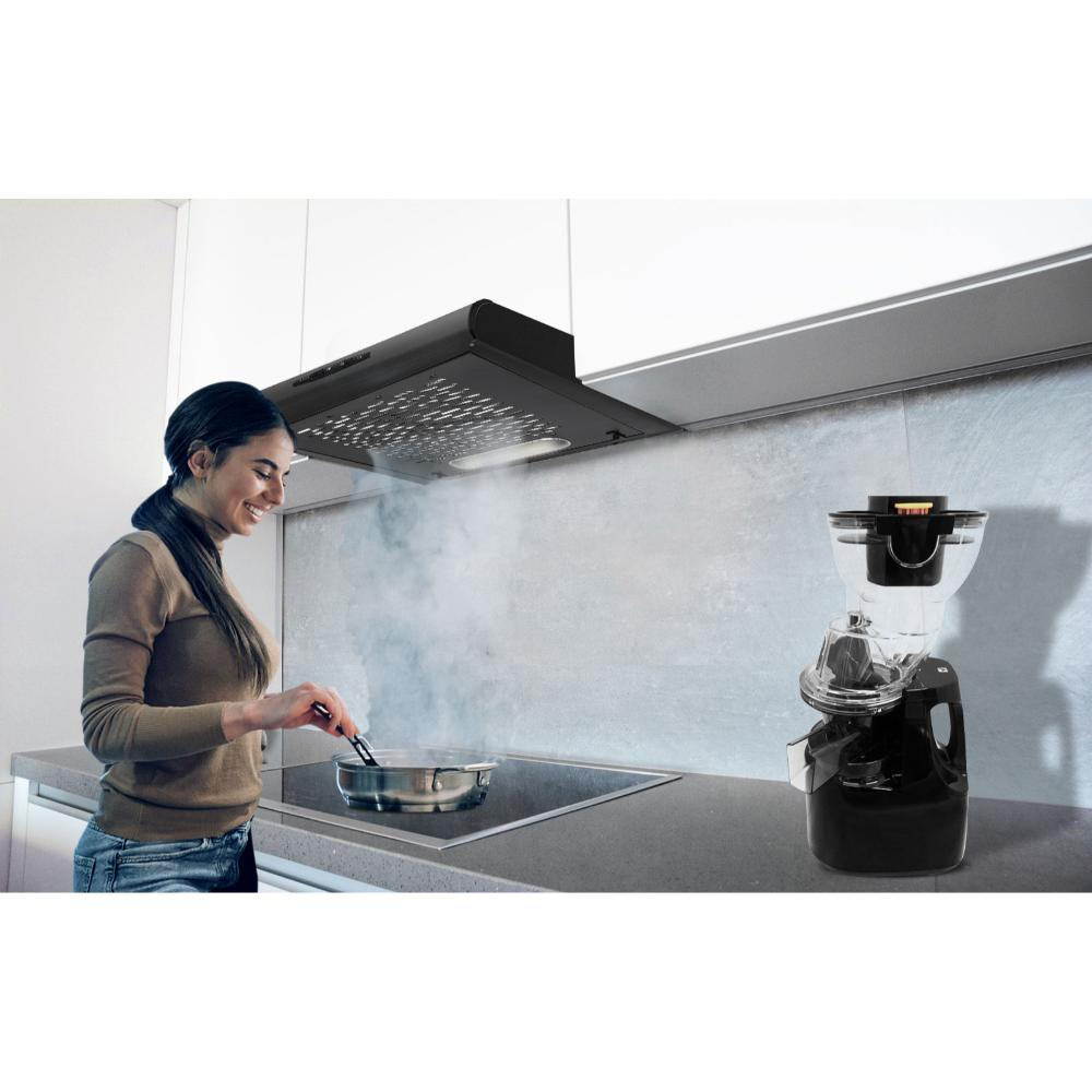 Una donna cucina in una cucina. Usa le pinze per mescolare il cibo in una padella su un piano cottura. Un macinacaffè è vicino.