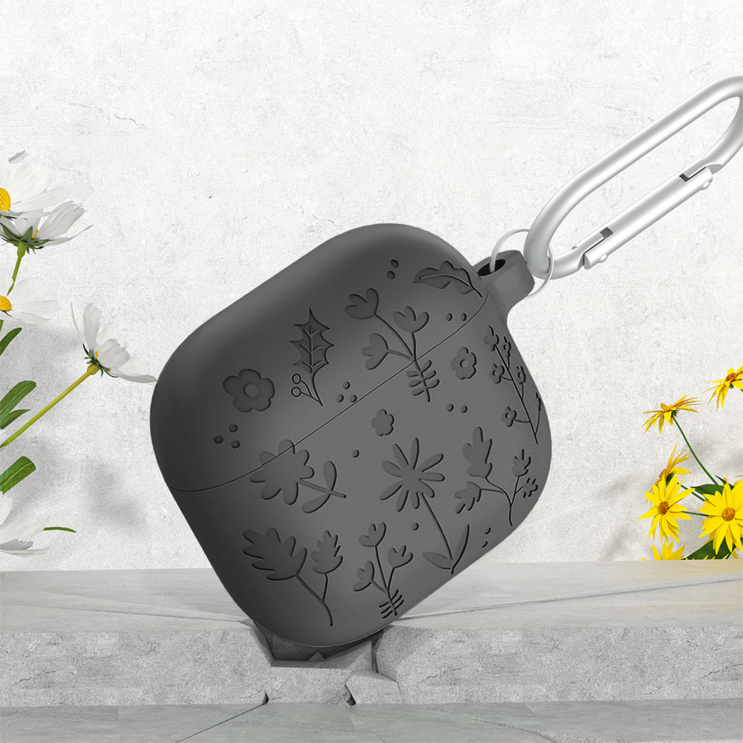 Una funda gris oscuro para AirPods con diseños florales, mosquetón plateado, margaritas y flores amarillas.
