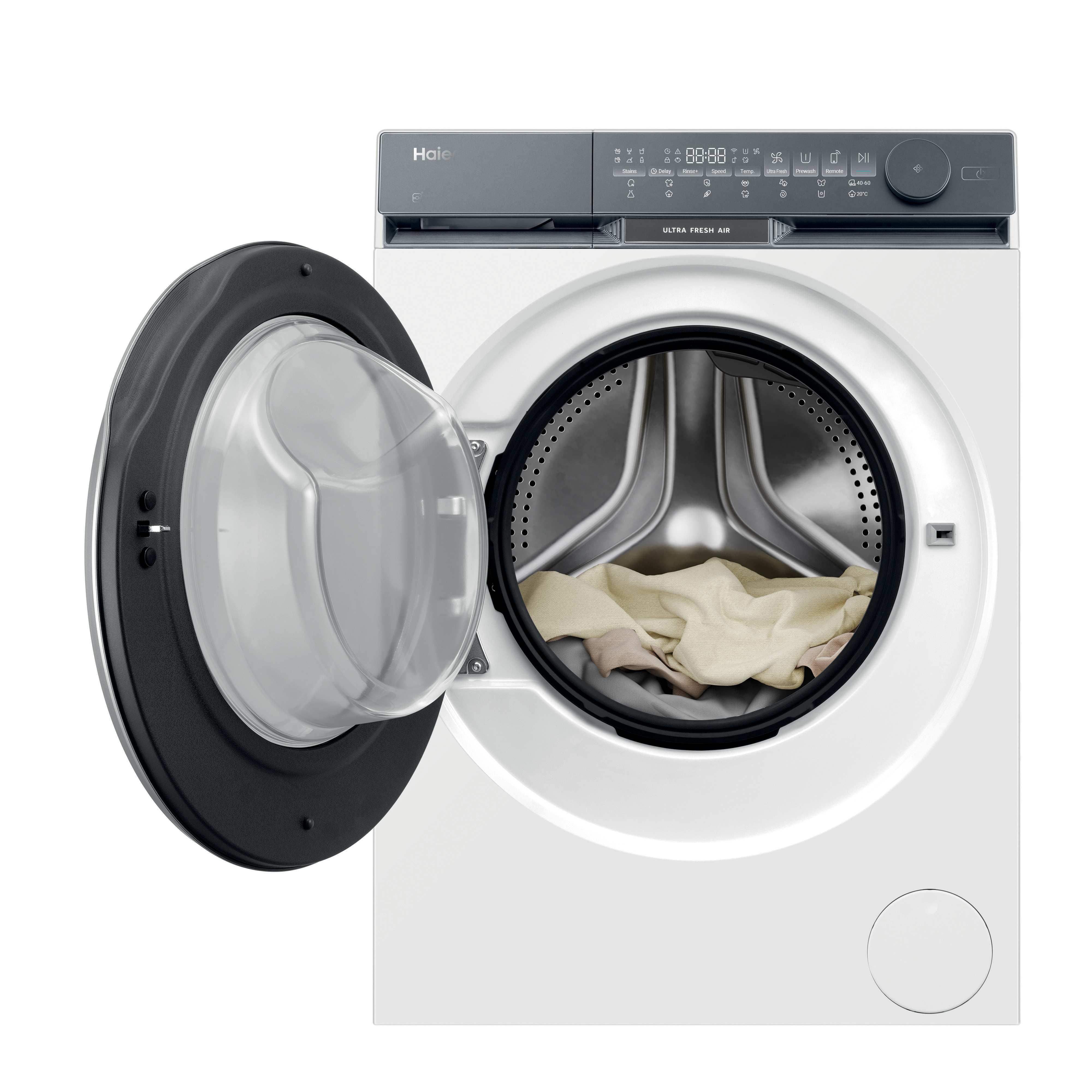 Una lavadora Haier blanca con la puerta abierta, mostrando ropa dentro. El panel de control es gris.