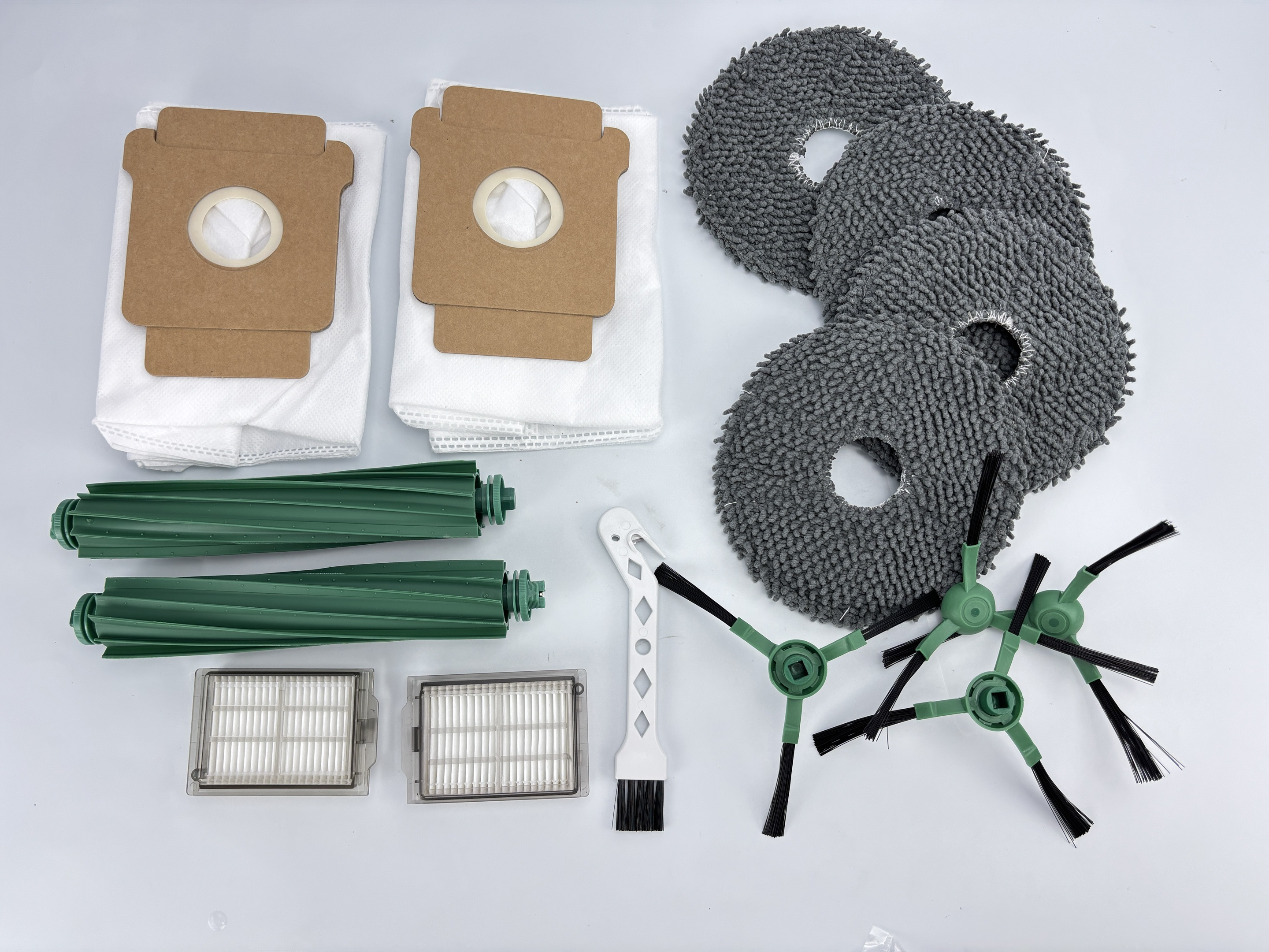 Parti di robot aspirapolvere: filtri, spazzole, tamponi e sacchetti, disposti su una superficie bianca. Vari colori e forme.