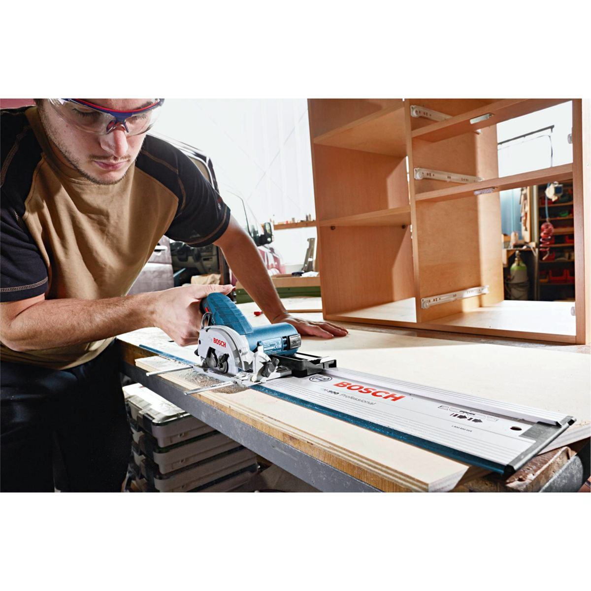 Un hombre usa una sierra circular en una tabla de madera. Un armario parcialmente construido está en el fondo. La sierra es azul y blanca.