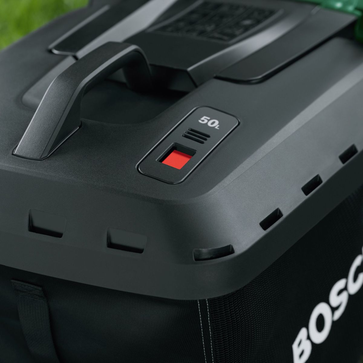 Primer plano de la parte superior de un cortacésped negro con asa y botón rojo. La bolsa tiene el logo 'Bosch'.