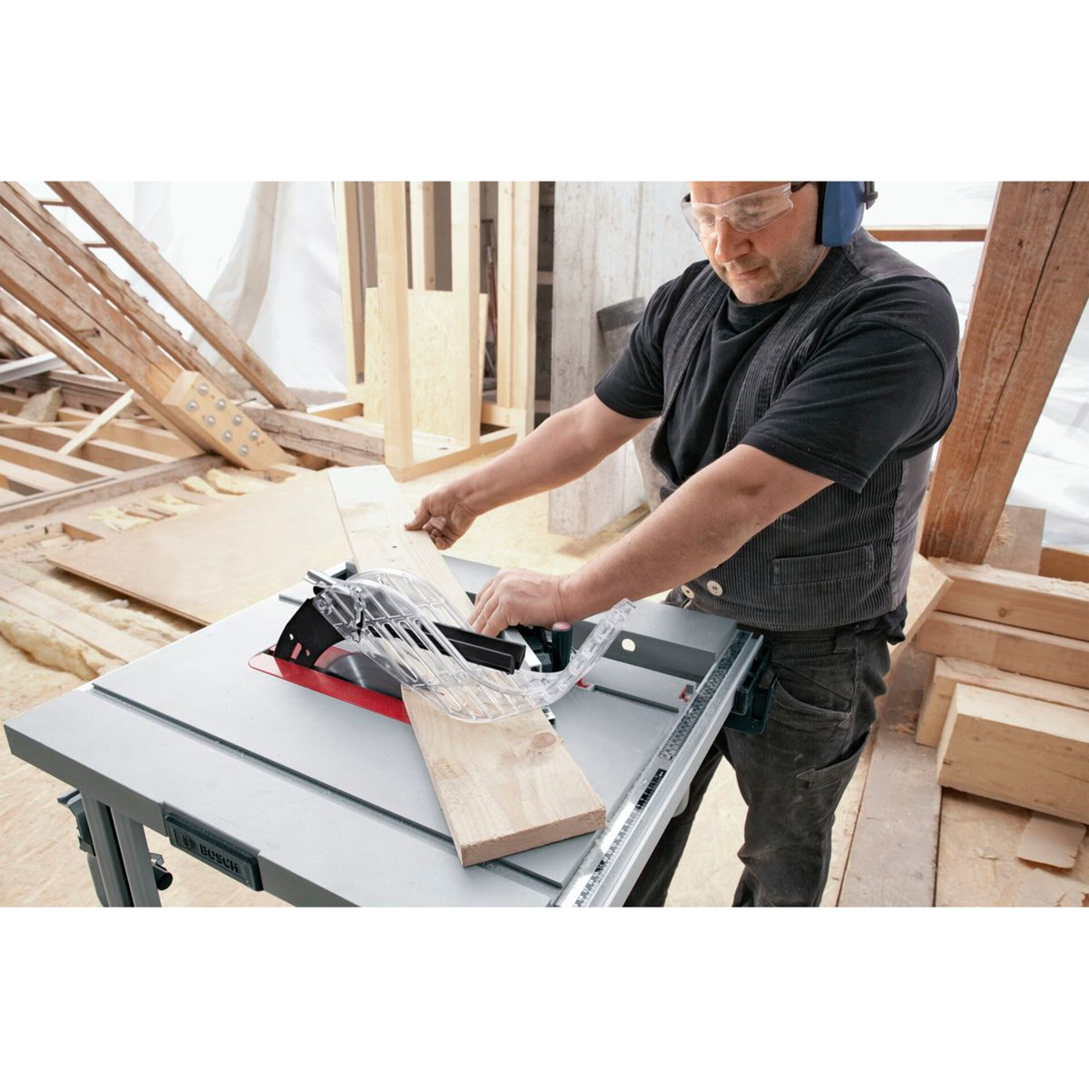 Un hombre usa una sierra de mesa para cortar madera. Usa gafas y protección auditiva. El fondo muestra una construcción.