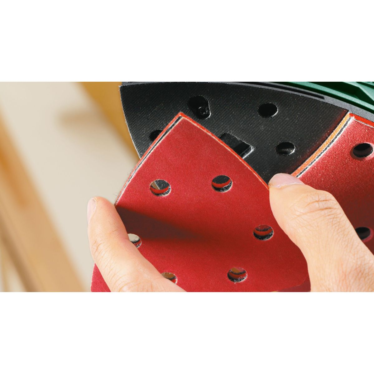 Main tenant du papier de verre rouge. Dos noir avec trous. Surface en bois en arrière-plan.