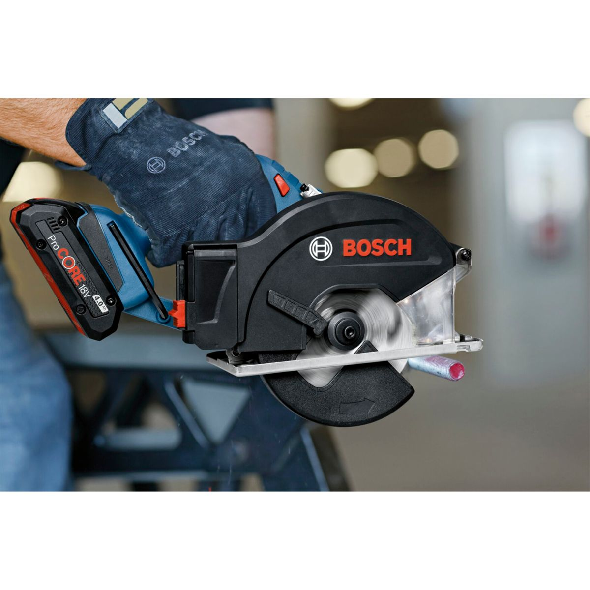 Una mano guantata aziona una sega circolare Bosch, tagliando una barra di metallo. La sega è nera e blu. Una batteria rossa è collegata.