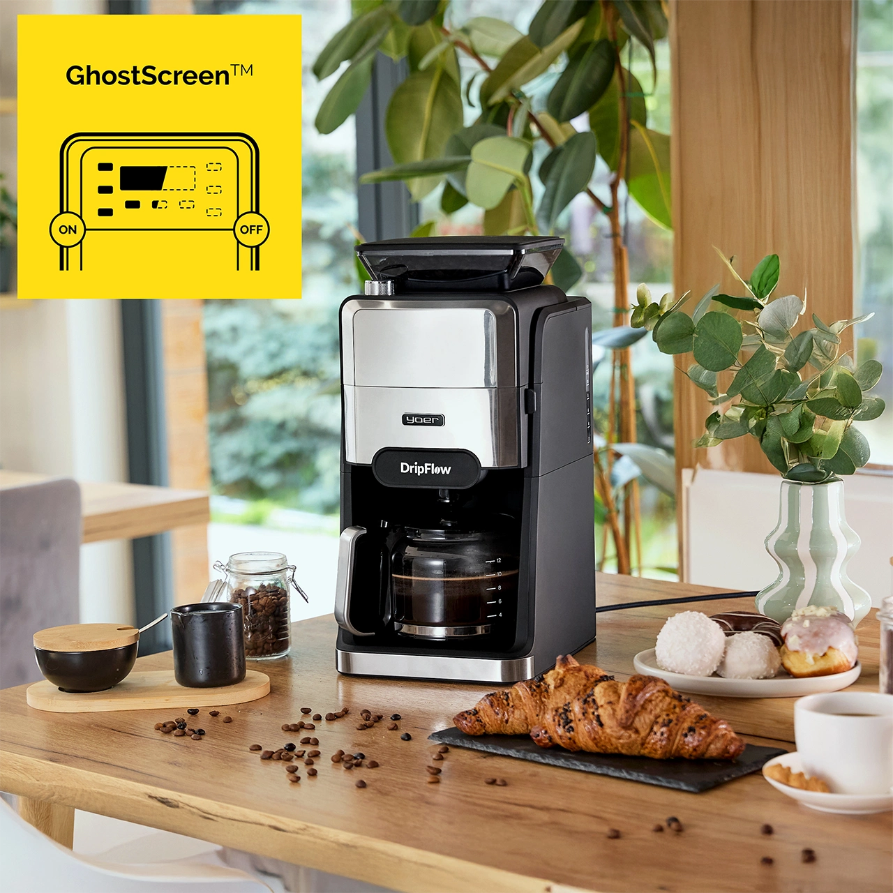 Ekspres do kawy z rogalikiem, pączkami i kawą na drewnianym stole. W tle wazon z liśćmi.