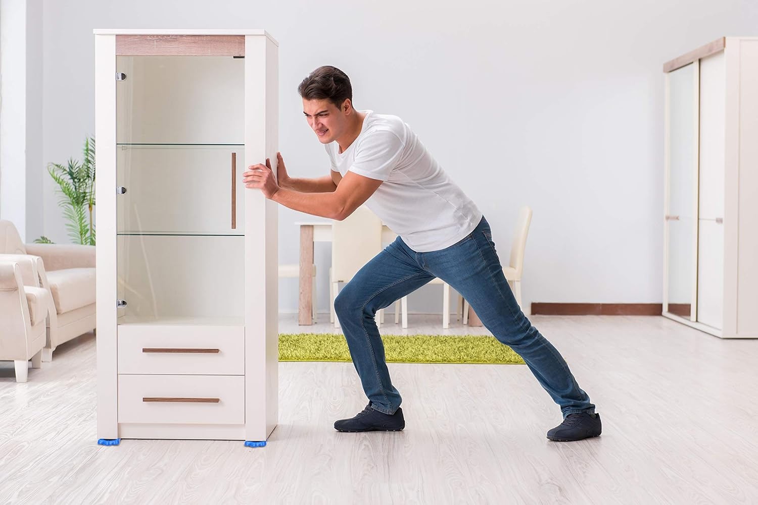 Ein Mann in Jeans und weißem Hemd schiebt einen weißen Schrank. Der Raum hat einen grünen Teppich, ein Sofa und einen weißen Schrank.