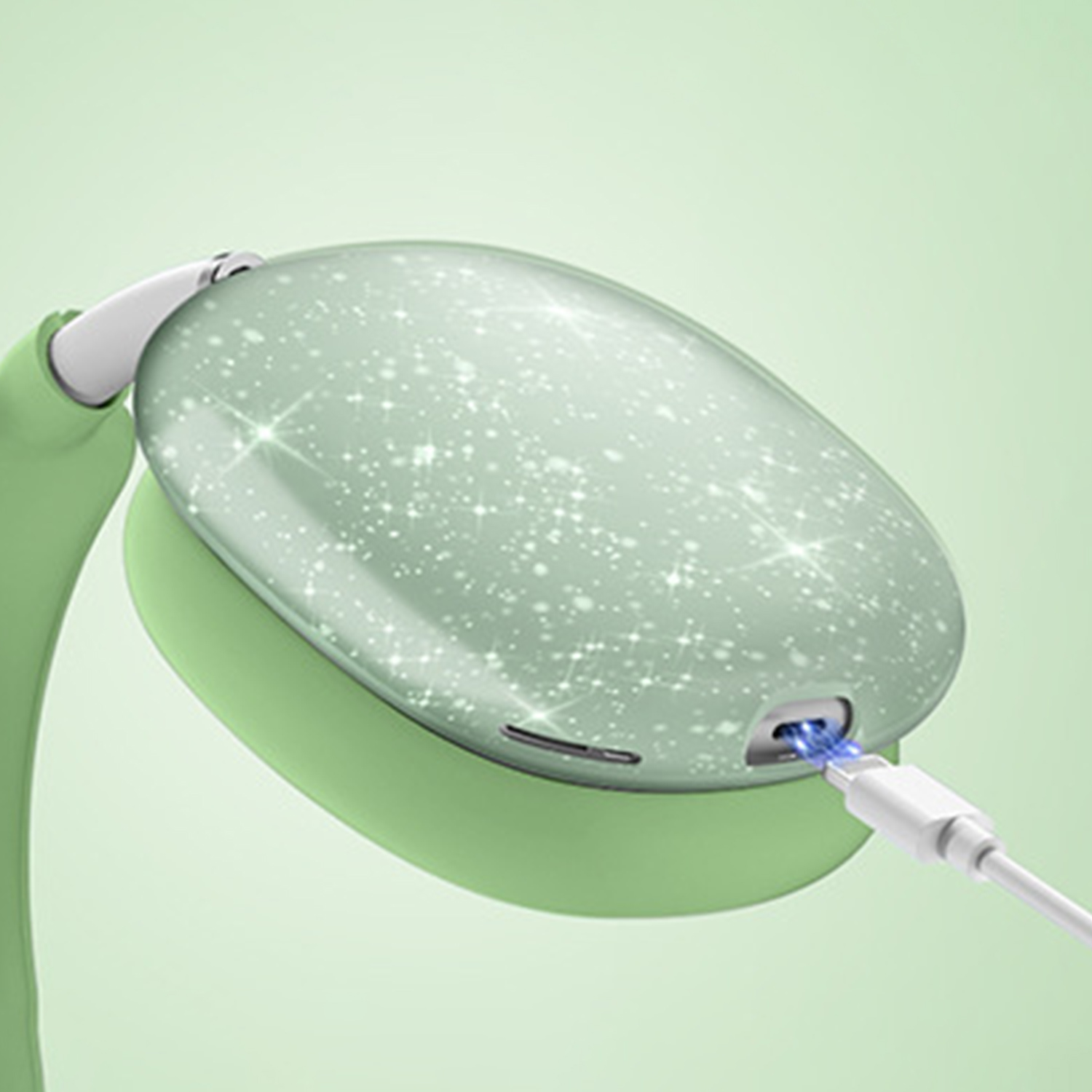 Cuffie verdi con un design stellato vengono caricate con un cavo bianco. Lo sfondo è una sfumatura verde chiaro.