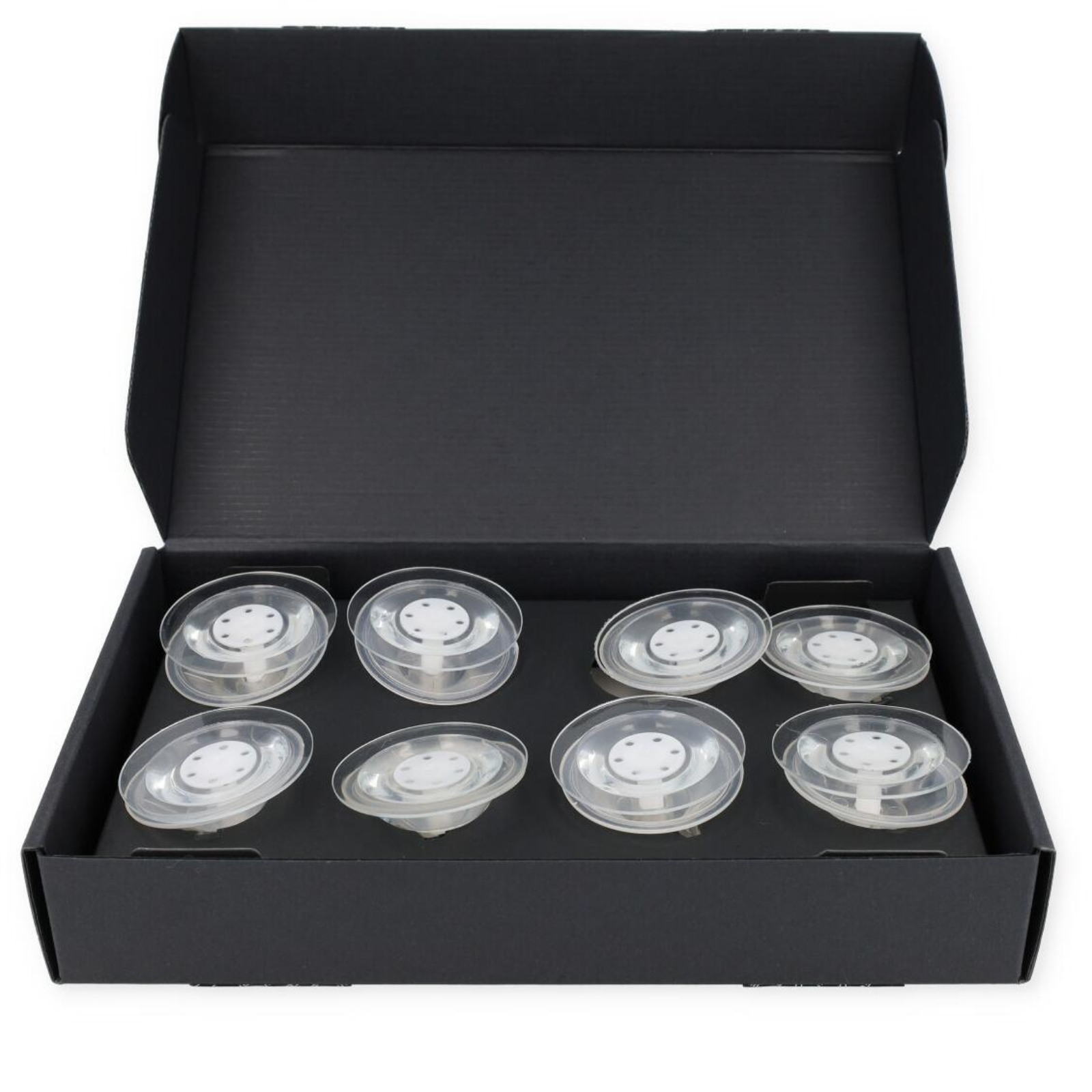 Otwarta czarna skrzynka zawiera osiem przezroczystych plastikowych przedmiotów z białymi środkami, ułożonych w dwóch rzędach. Białe tło.