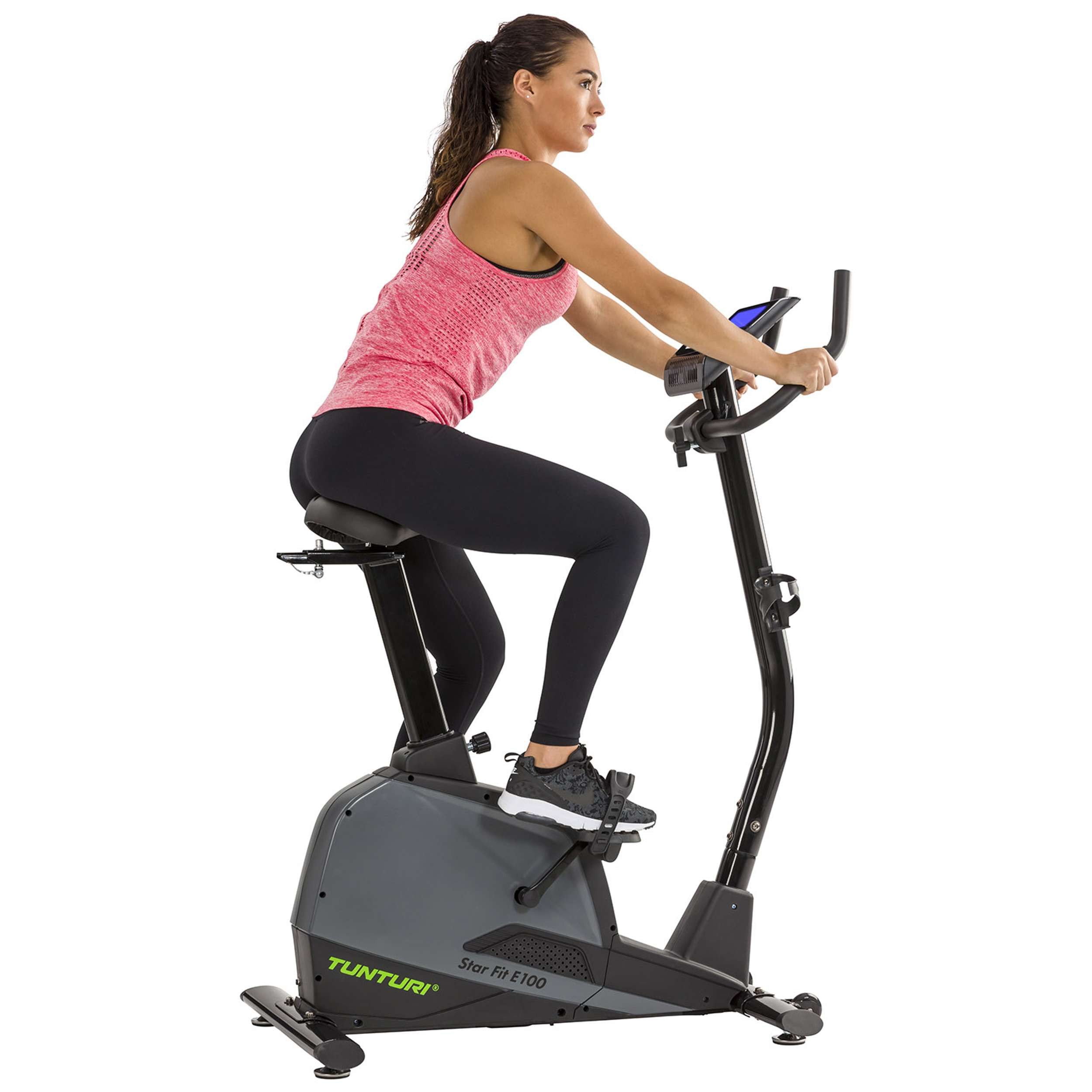 Vrouw op hometrainer. Ze draagt een roze top en zwarte legging. Fiets is grijs en zwart. Achtergrond is wit.