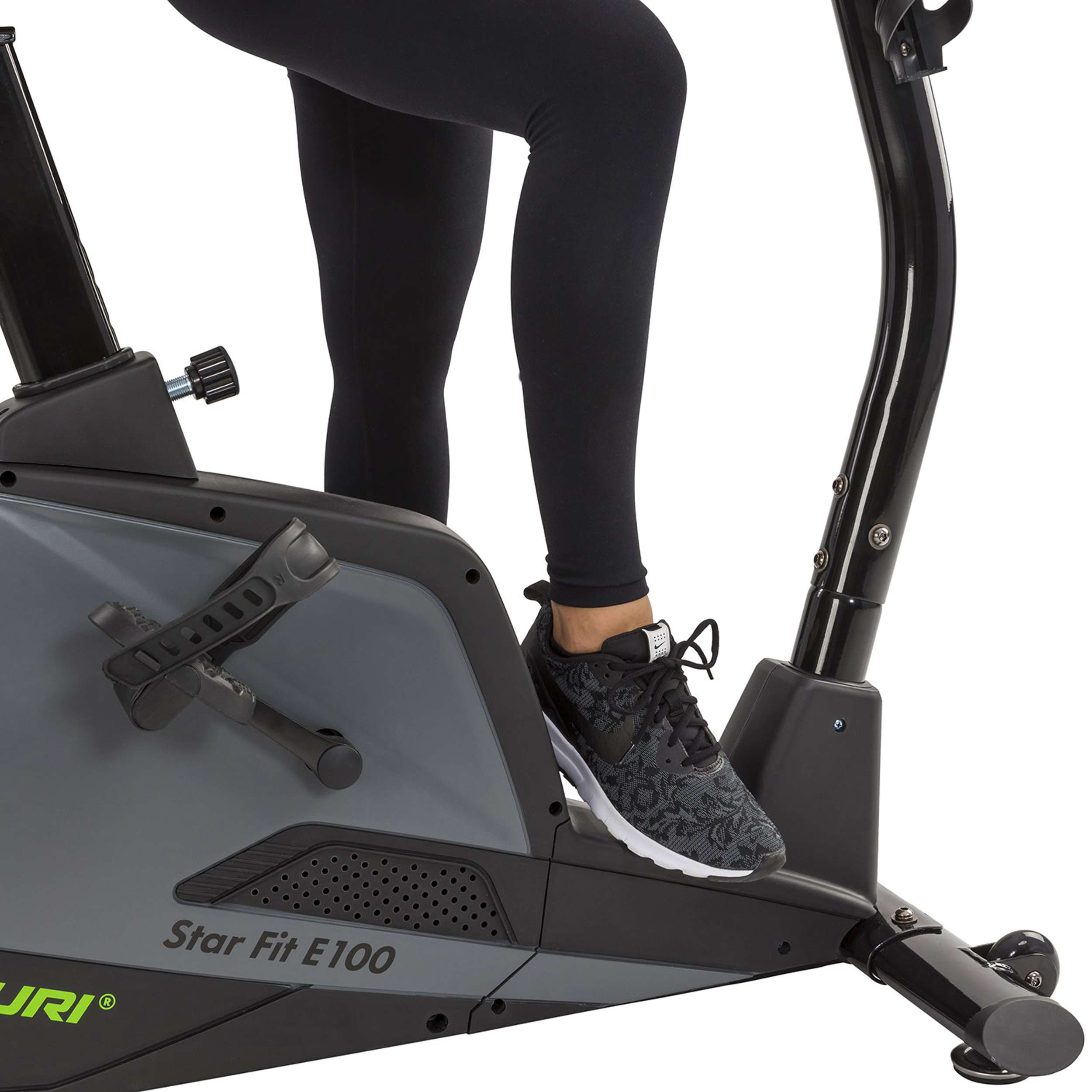 Benen en voet van een persoon op een hometrainer. De fiets is zwart en grijs. De persoon draagt een zwarte legging en een schoen met patroon.
